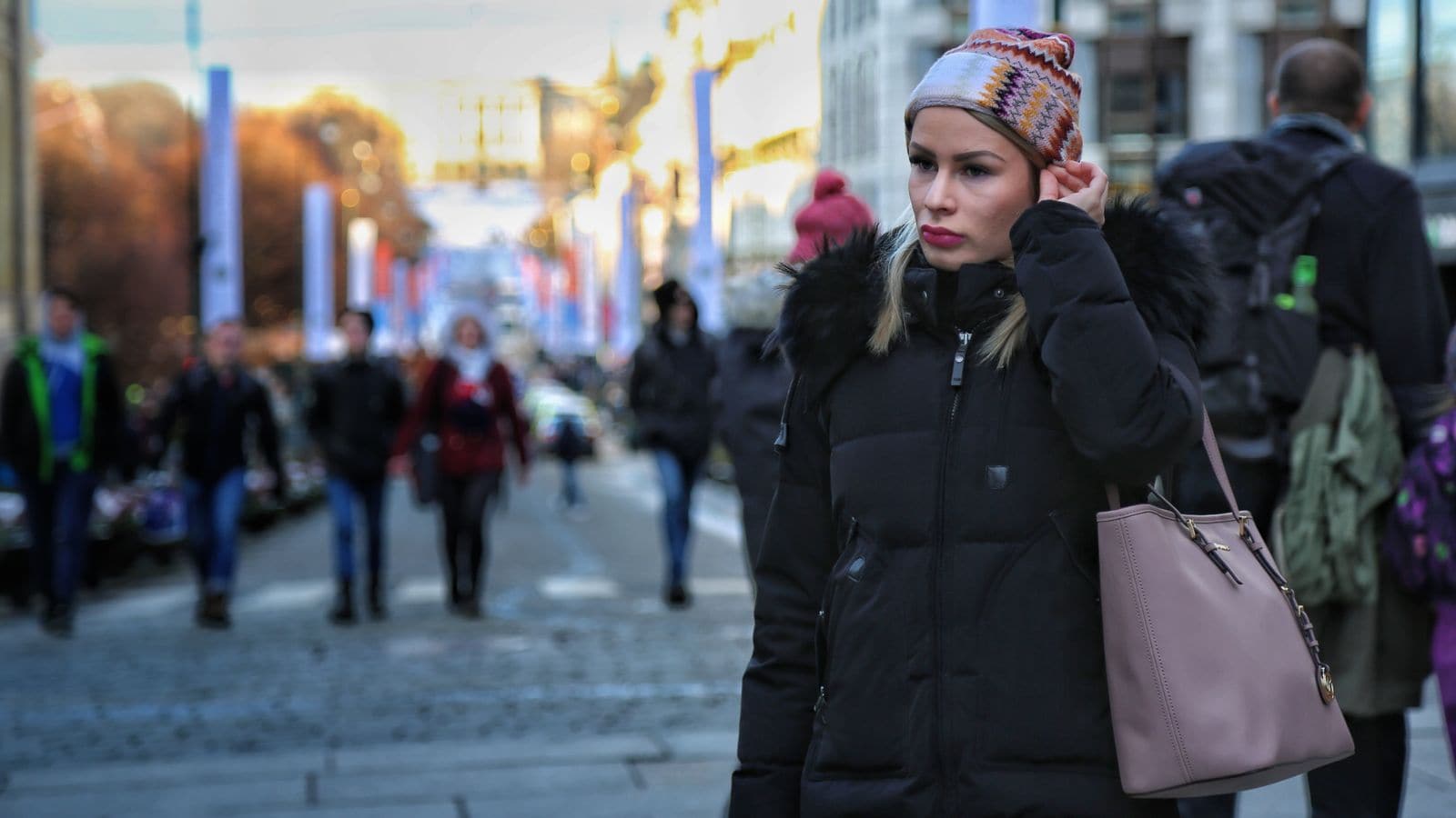Ung kvinne på Karl Johans gate i Oslo hvor slottet skimtes i bakgrunnen. Hun har vinterklær på seg - topptue og jakke med pelskrage og ser litt ettertenksom ut.