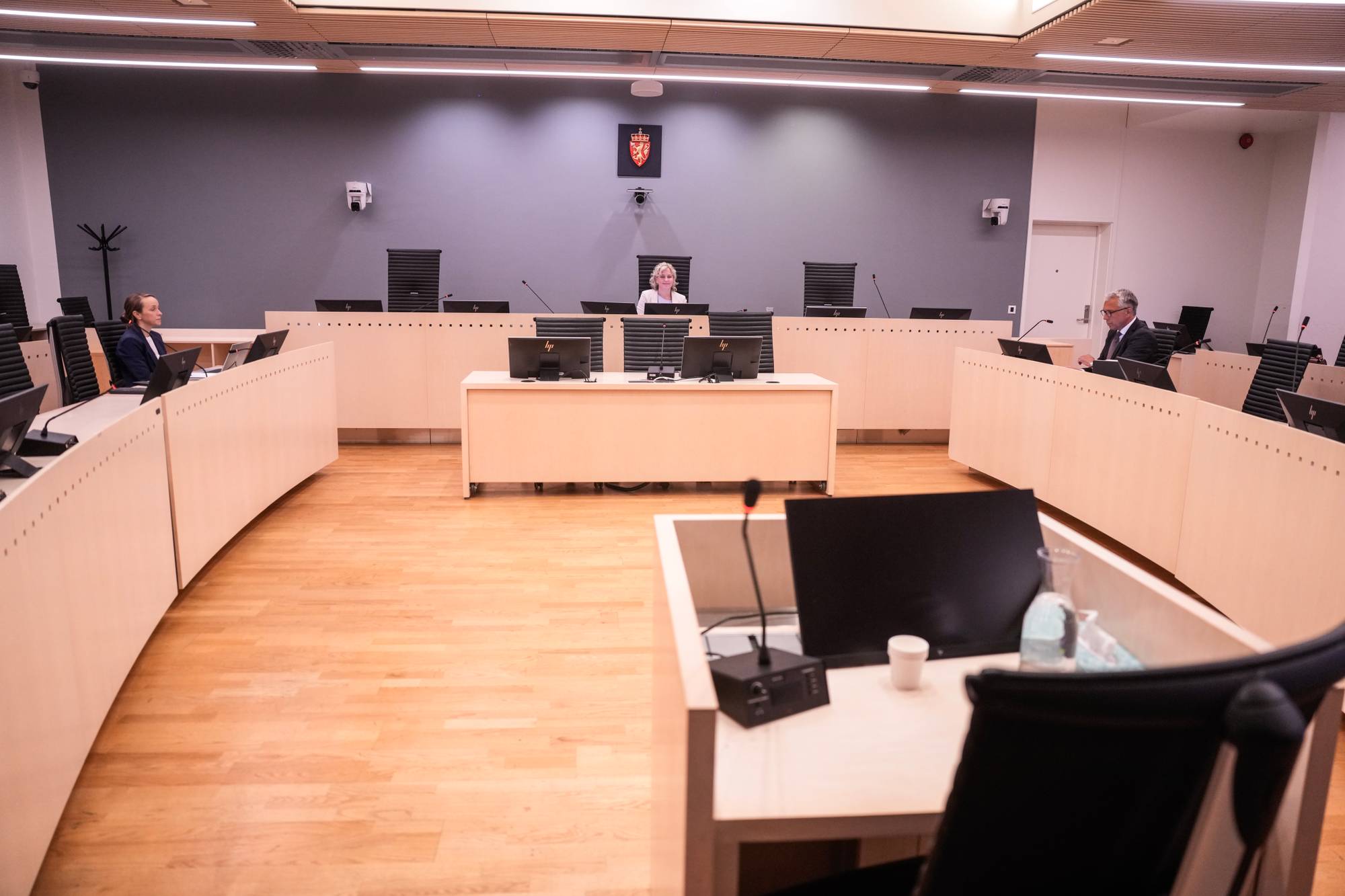 Rettssal med dommer i midten og advokater ved sidene. Våpenskjold på veggen i bakgrunnen. (Bildebeskrivelsen er laget av en KI-tjeneste)