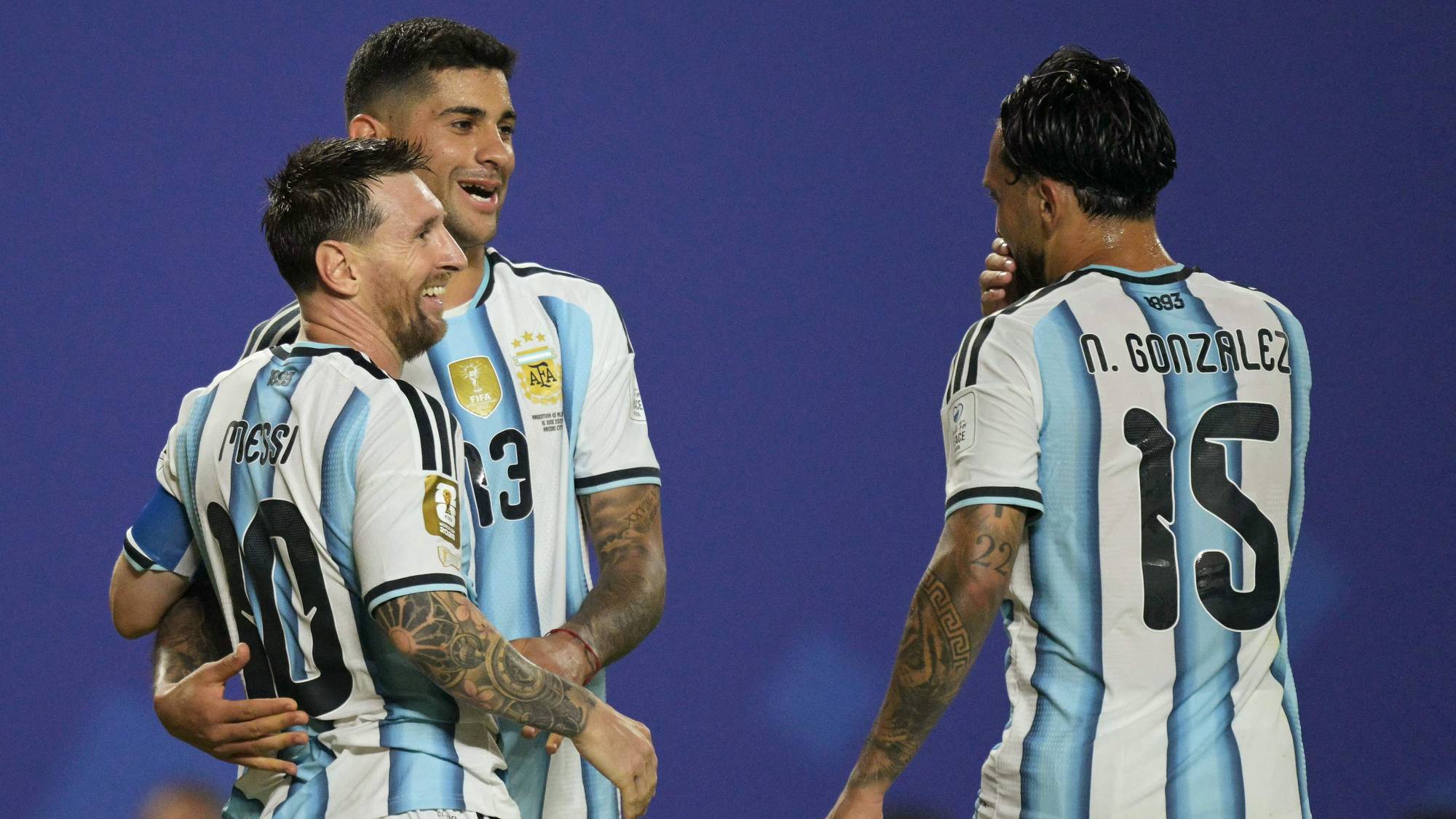 Lionel Messi, Lisandro Martínez og Nicolás González fra Argentina feirer. De er ikledd Argentinas drakt med lyseblå og hvite striper. Bildet er tatt på en blå bakgrunn. (Bildebeskrivelsen er laget av en KI-tjeneste)