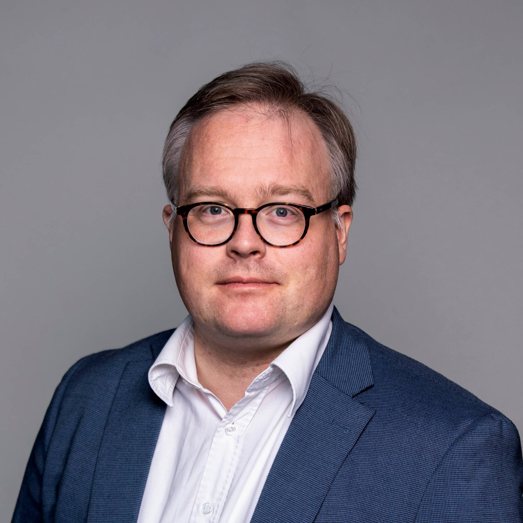 Mann med briller, skjorte og dressjakke.