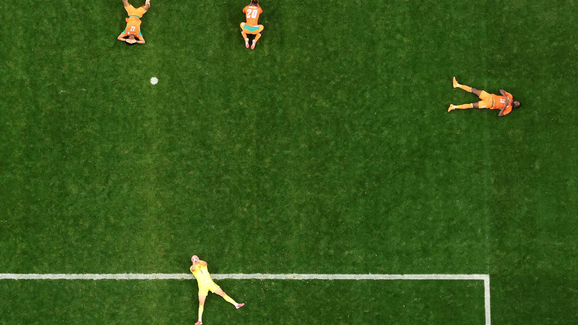 Fotballspillere ligger utslitte på gresset etter en kamp sett fra fugleperspektiv. (Bildebeskrivelsen er laget av en KI-tjeneste)