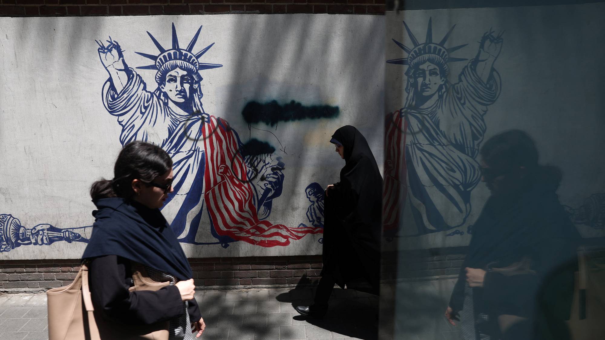 To personer går forbi en anti-amerikansk vegg plakat i teheran