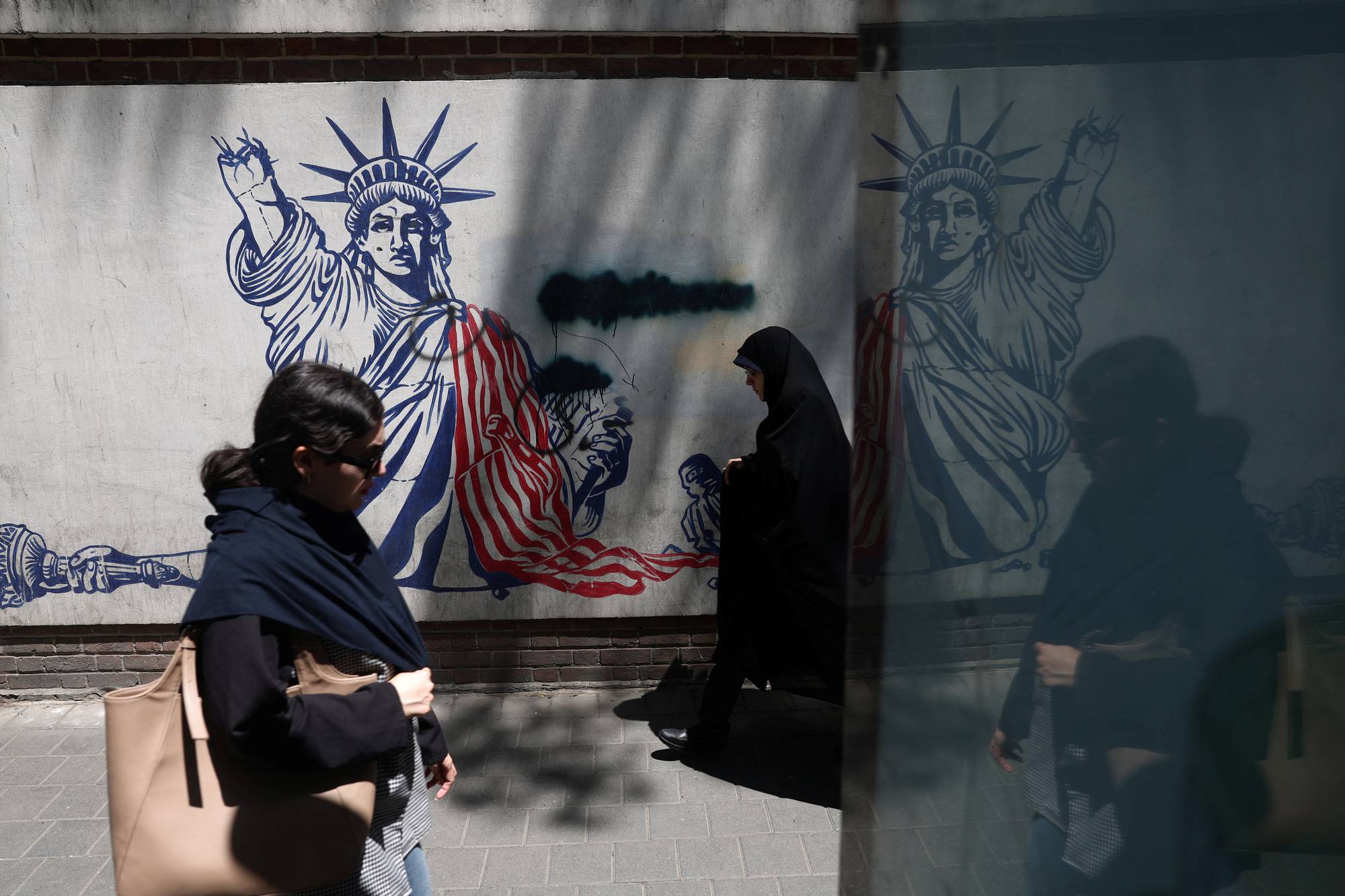 To personer går forbi en anti-amerikansk vegg plakat i teheran