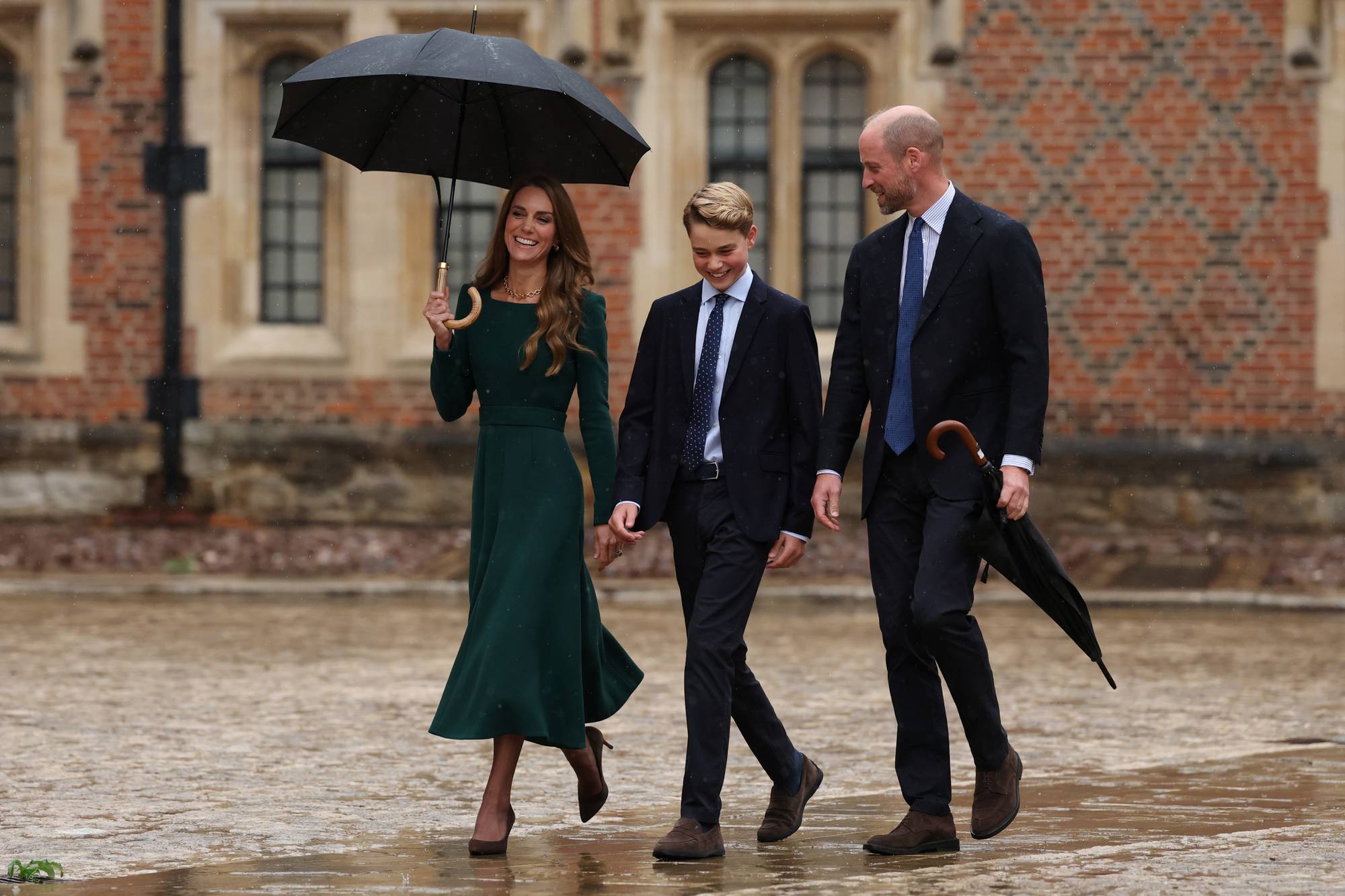 Prinsesse Catherine, prins George og prins William går sammen utendørs med en paraply. (Bildebeskrivelsen er laget av en KI-tjeneste)