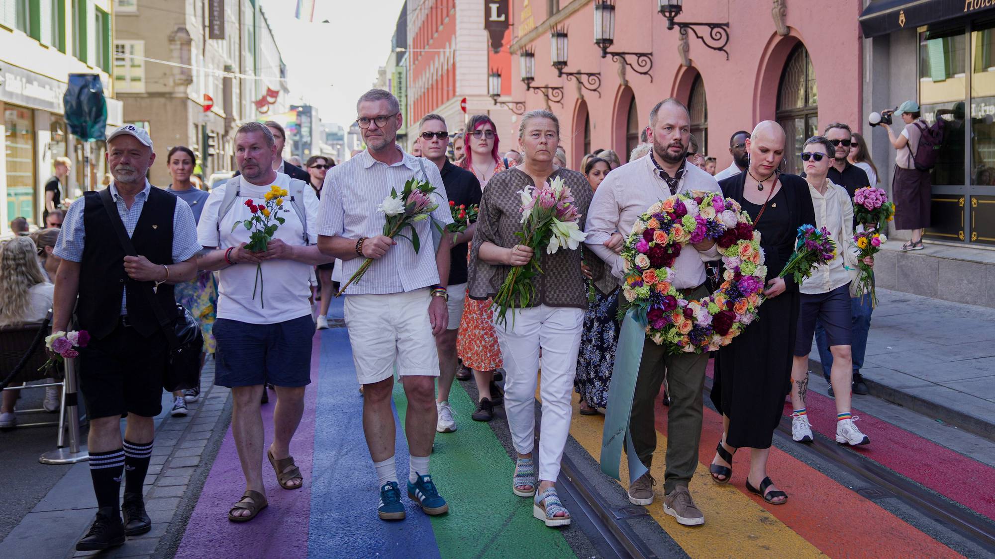En gruppe mennesker går i tog og holder blomster langs en regnbuefarget vei