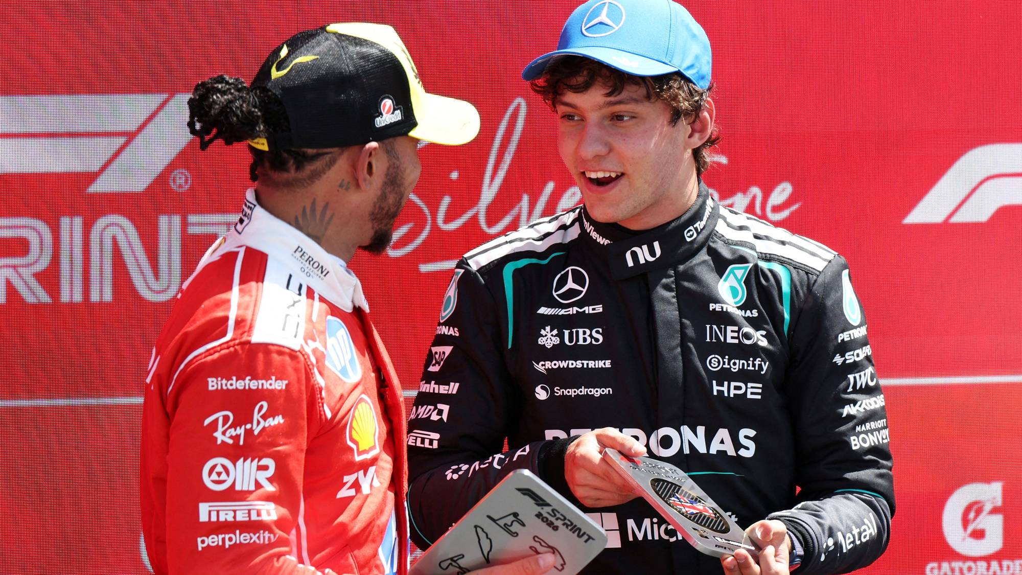Lewis Hamilton og Andrea Kimi Antonelli står foran en rød F1-bakgrunn med utmerkelser. (Bildebeskrivelsen er laget av en KI-tjeneste)