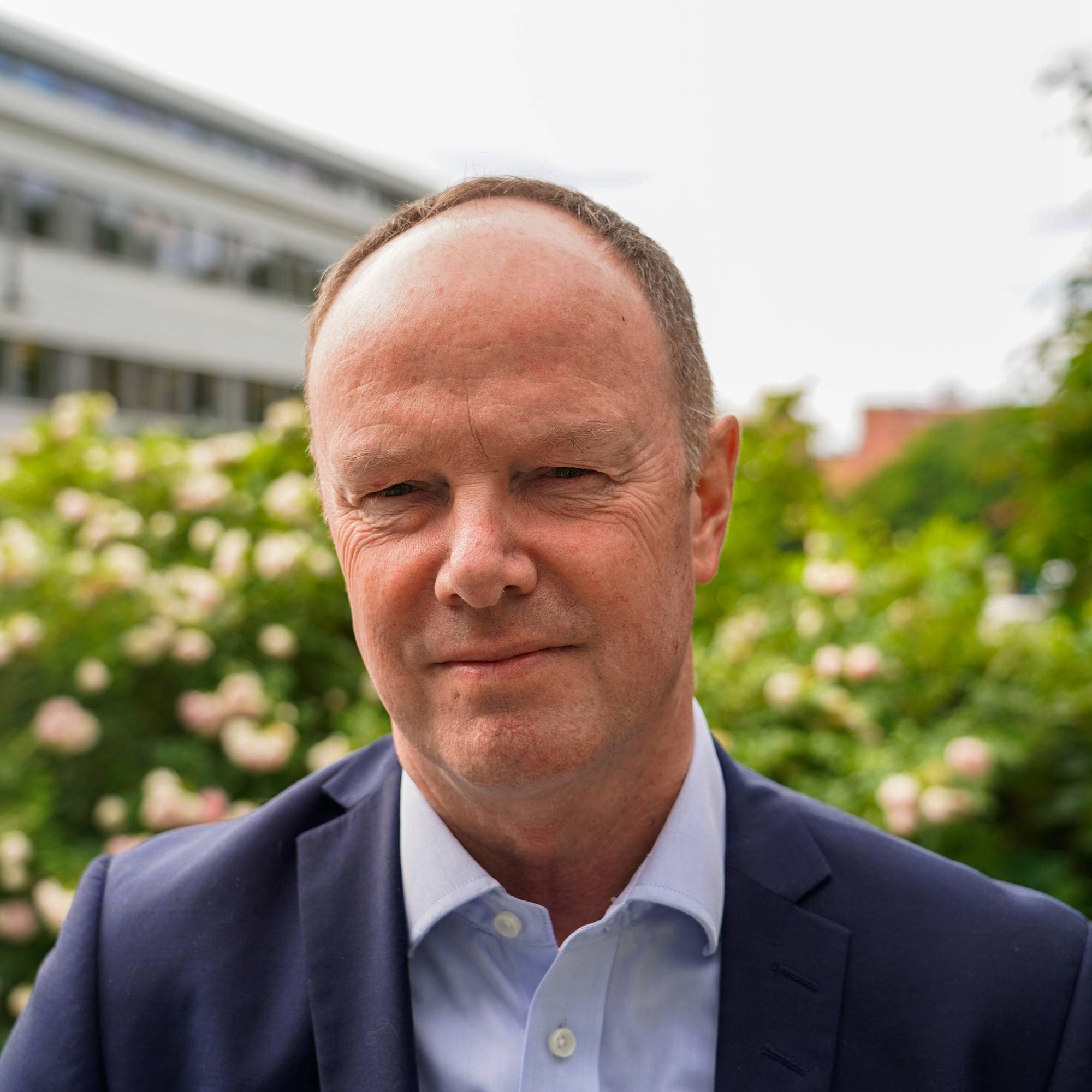 Mann med blå jakke og skjorte ser i kamera