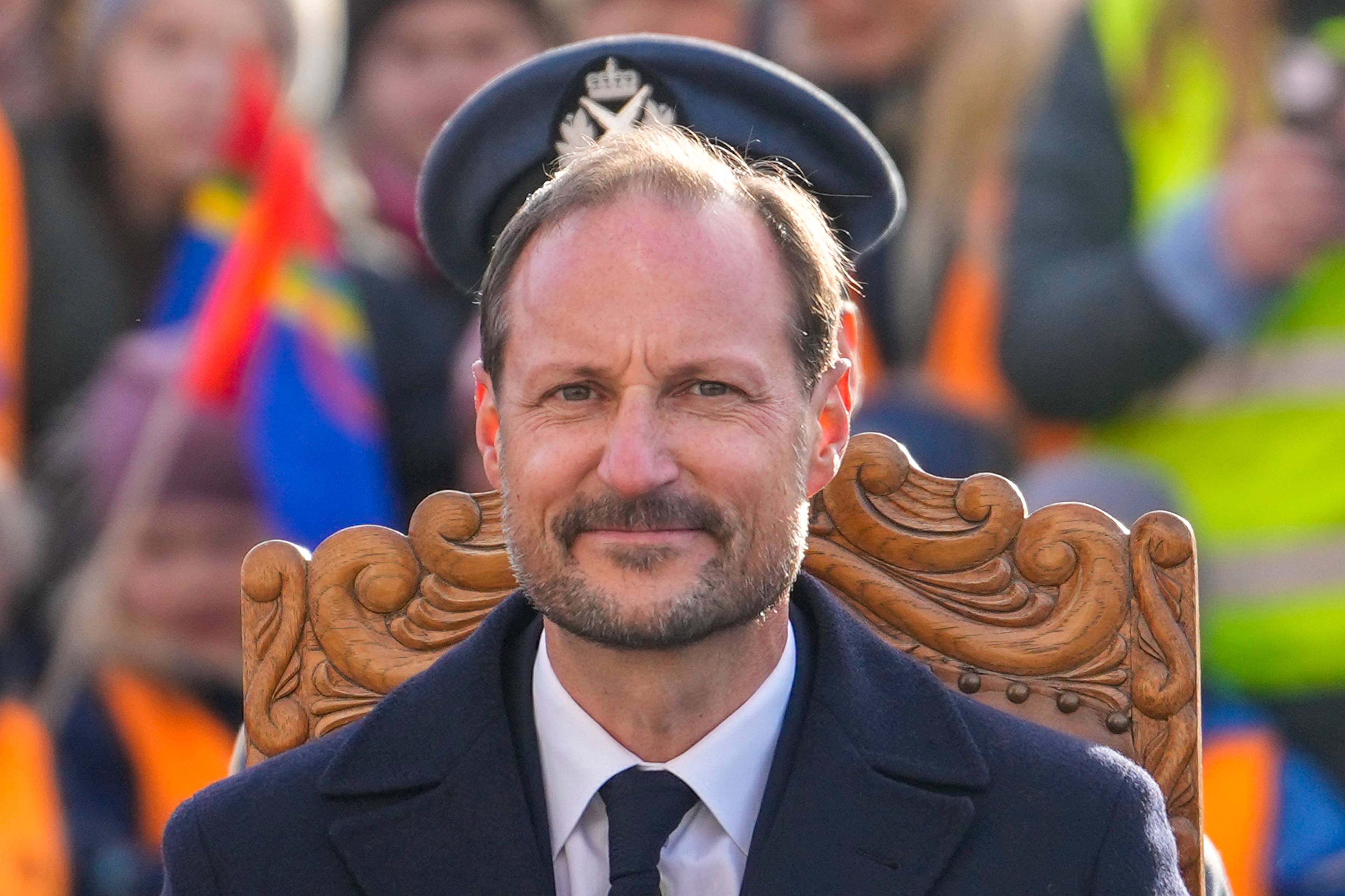 Kronprins Haakon sitter i en utskåret trestol iført uniformslue og mørk dress. Bakgrunnen er uklar. (Bildebeskrivelsen er laget av en KI-tjeneste)