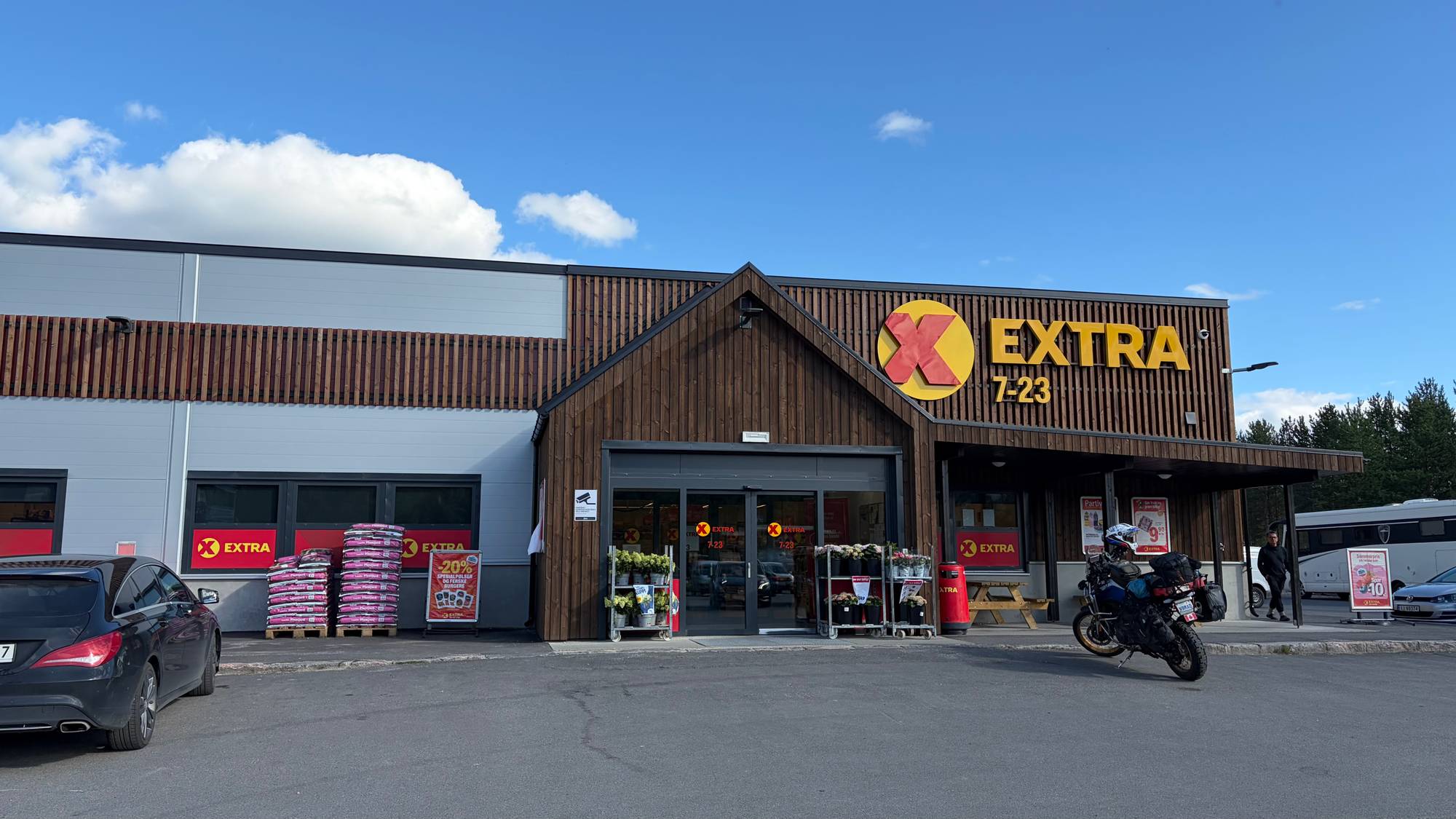 En Extra-dagligvarebutikk med parkeringsplass og inngangsparti under en blå himmel. (Bildebeskrivelsen er laget av en KI-tjeneste)