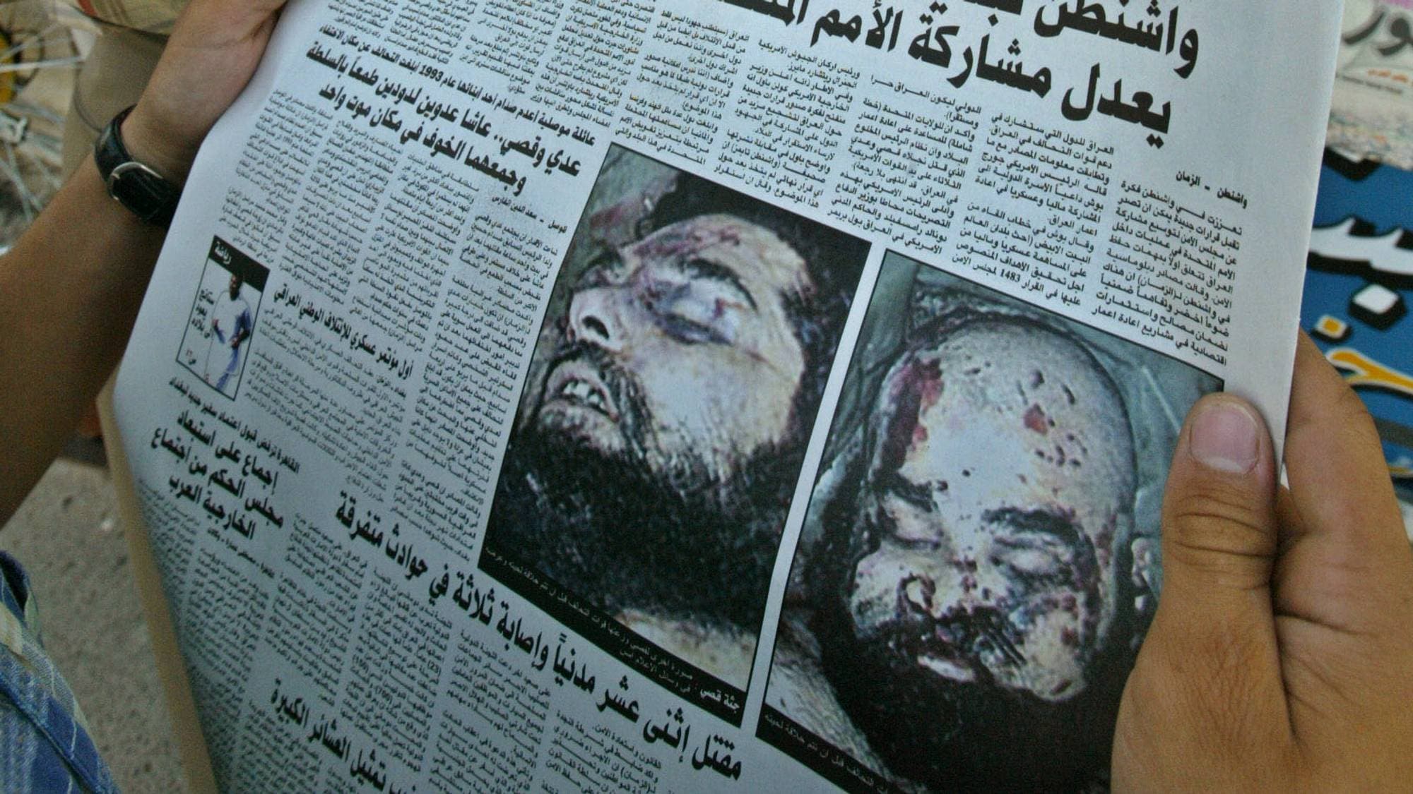 En mann holder opp en avis foran et nyhetsmedie. En annen mann leser også en avis. Avisen som holdes frem, har store arabiske bokstaver og bilder av døde menn. Det er mange aviser og nyhetsmedier i bakgrunnen. (Bildebeskrivelsen er laget av en KI-tjeneste)