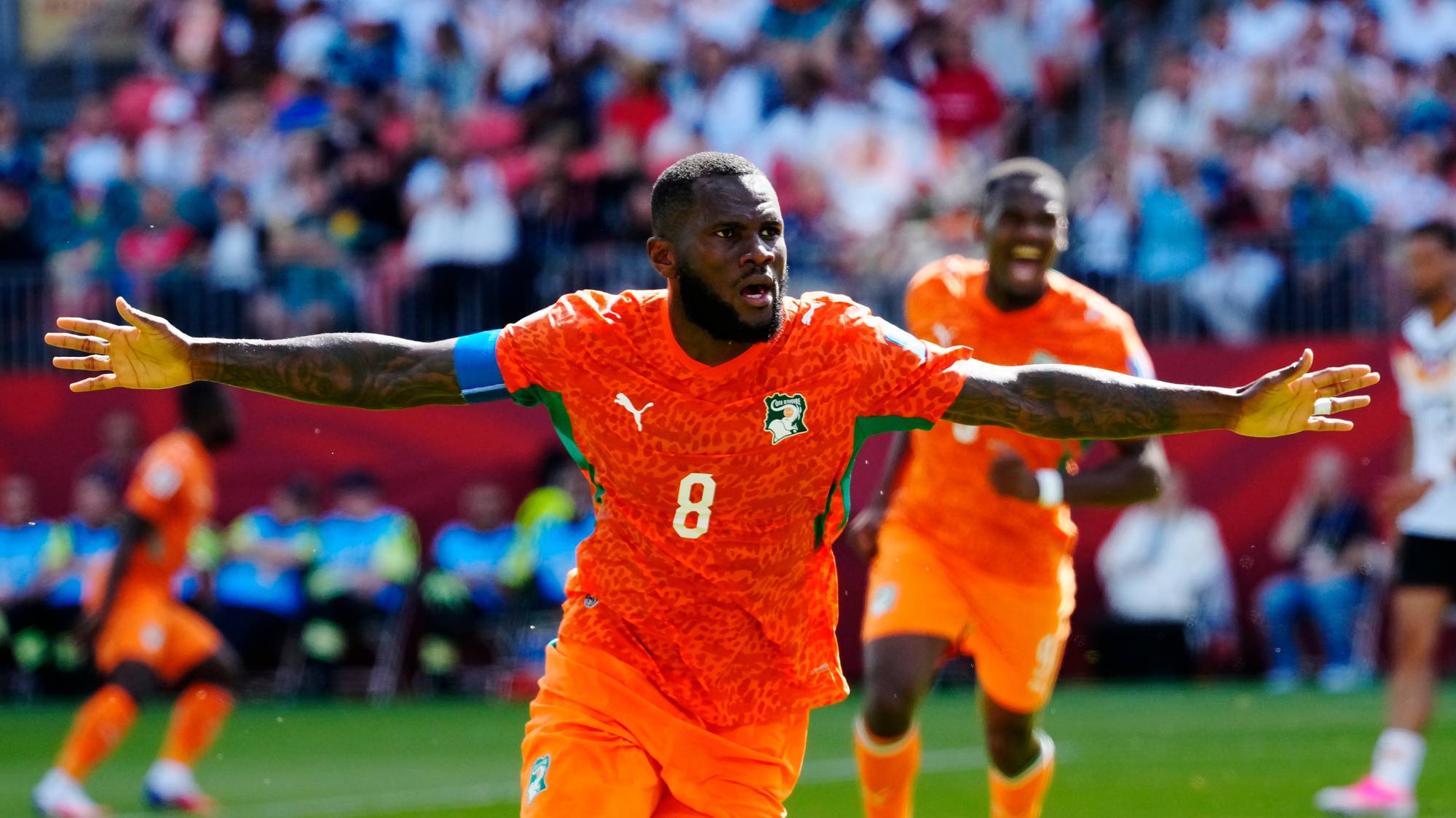 Franck Kessié feirer mål for Elfenbenskysten i oransje landslagsdrakt med armene strukket ut. 
