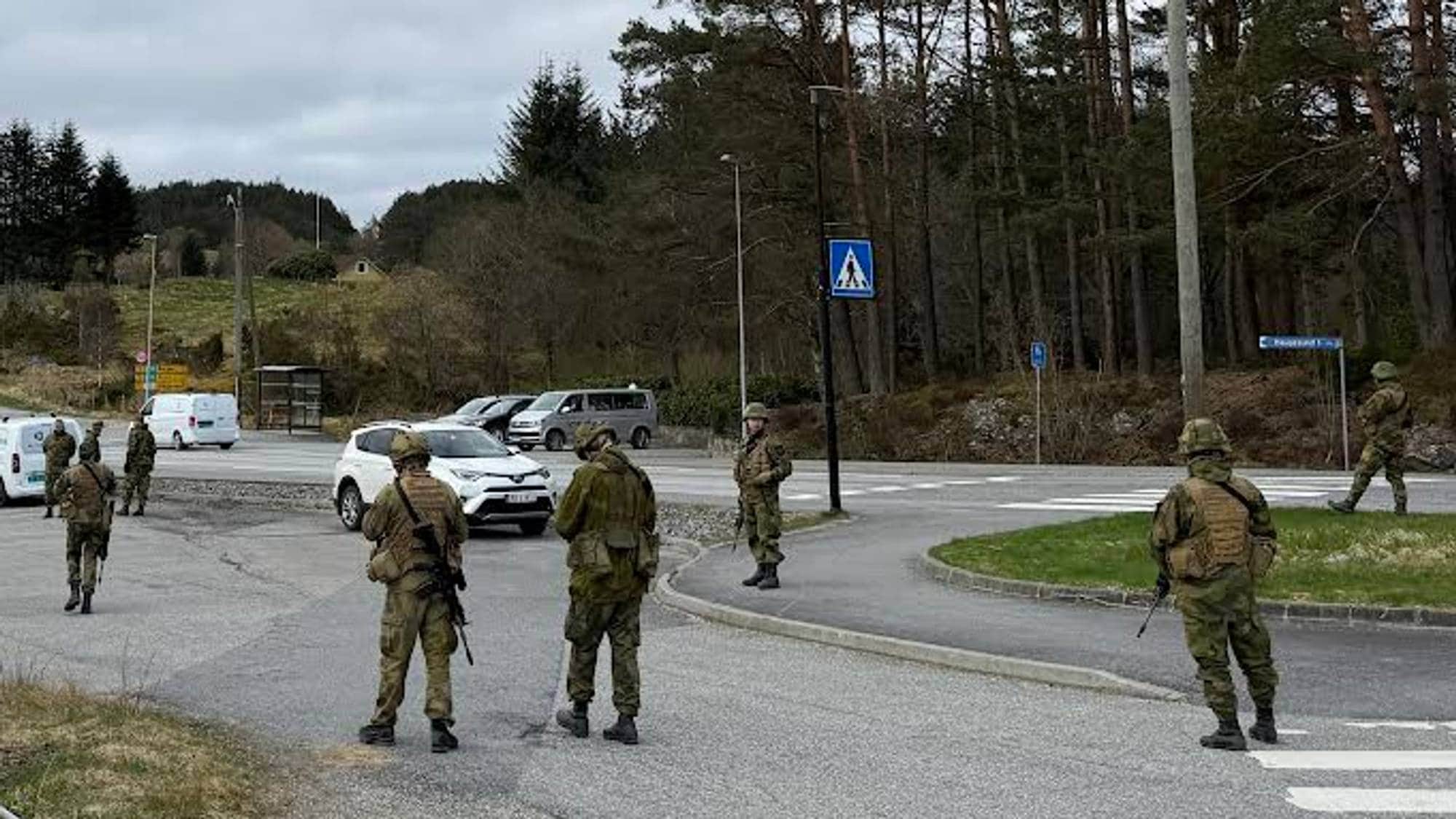 Heimevernøving i Sveio: ca 10 uniformerte soldatar fotograferte bakfrå, dei står spreidd på ein parkeringsplass langs ein veg.