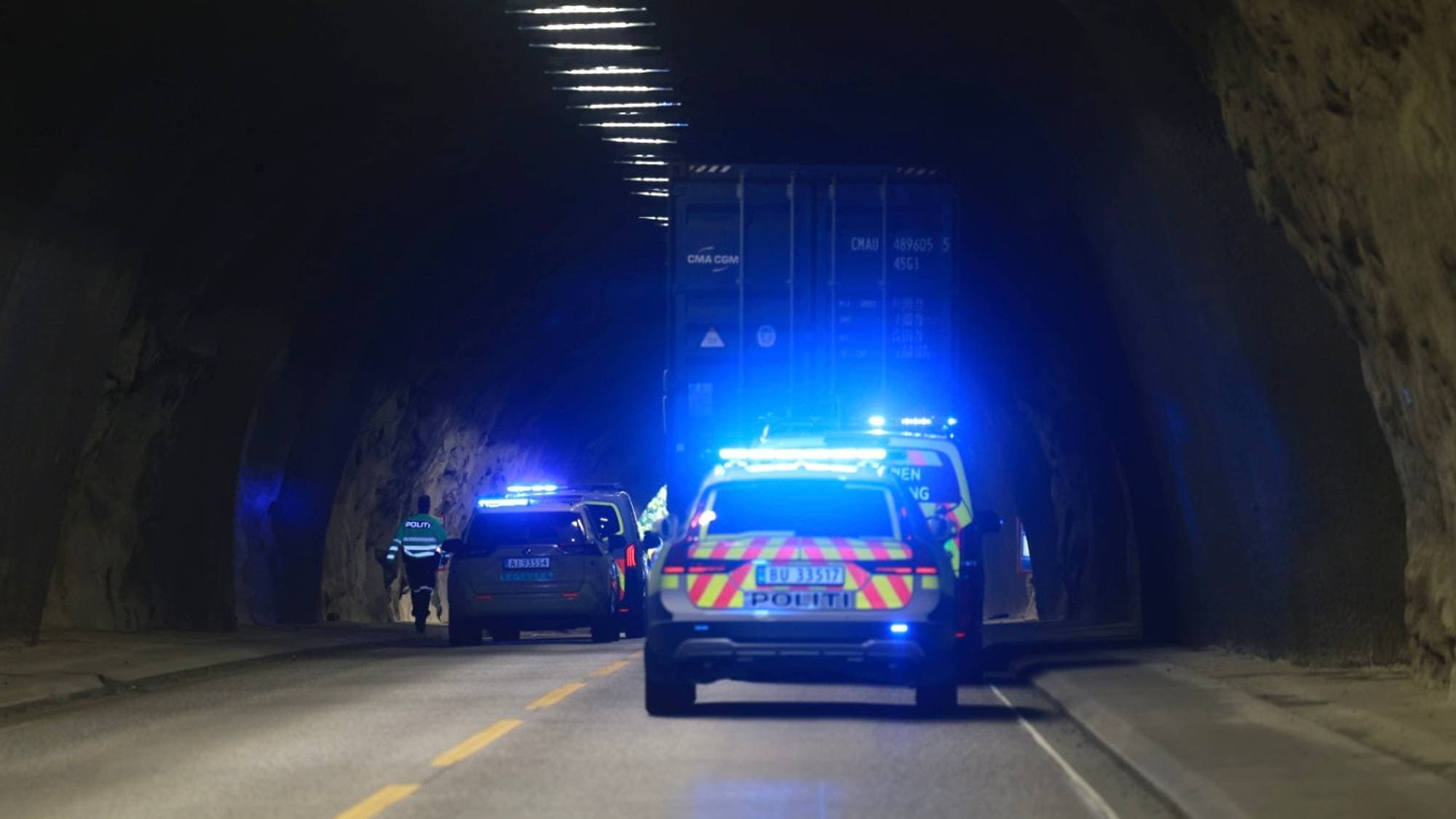 Politi og utrykningskjøretøy står ved en lastebil i en tunnel med blålys på. (Bildebeskrivelsen er laget av en KI-tjeneste)