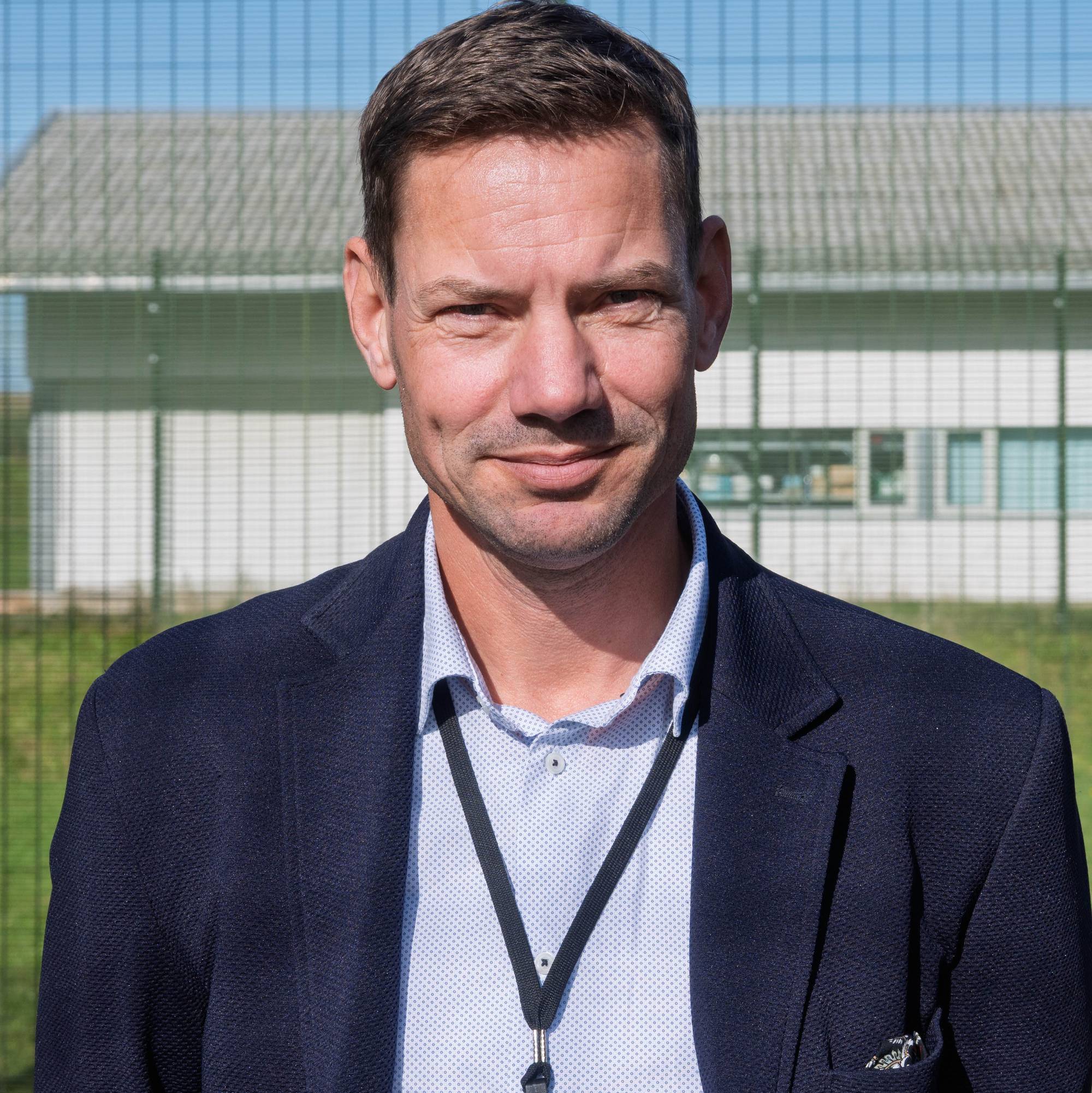 Mann i dress og skjorte foran et gjerde i en luftegård i et fengsel.