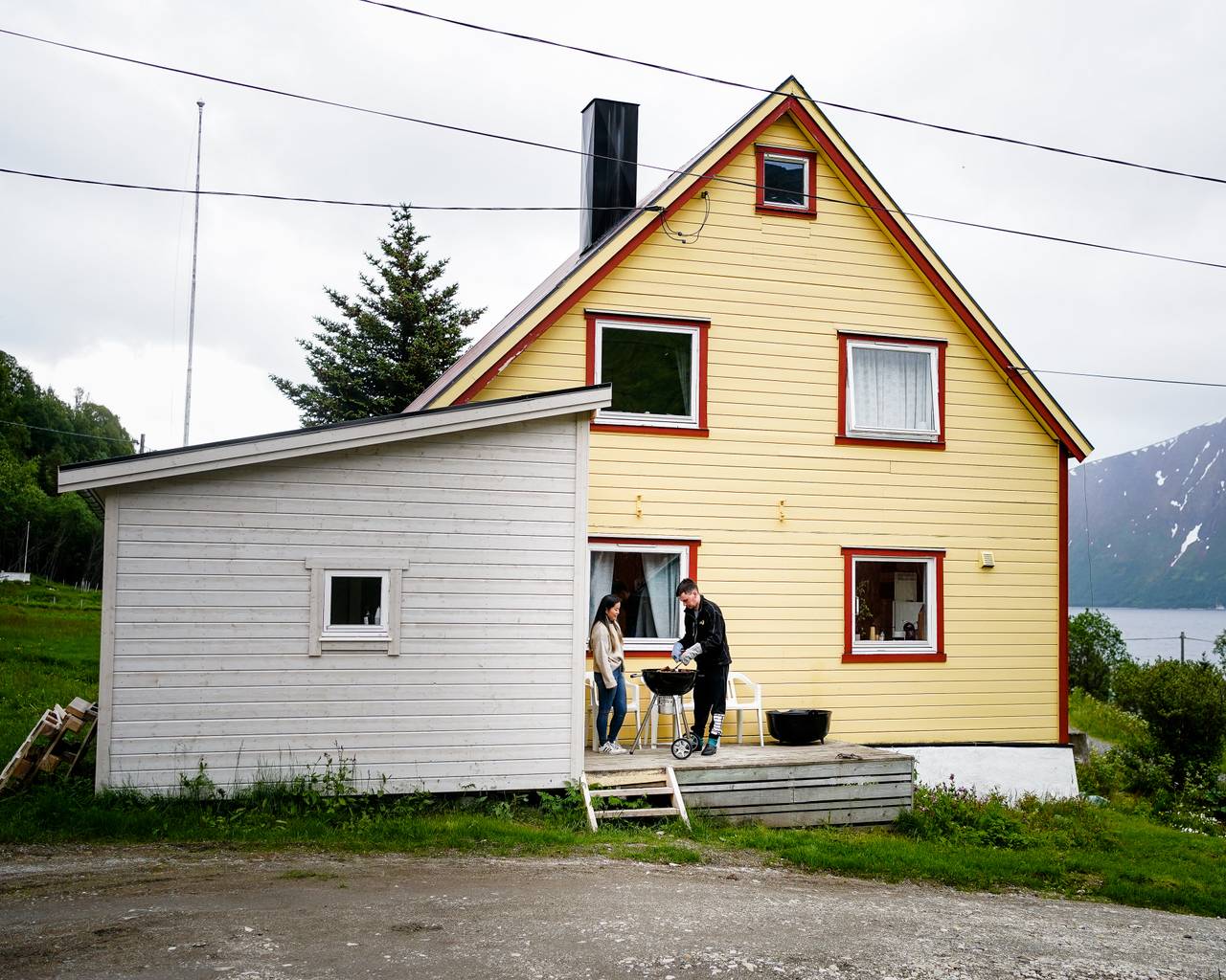 Ann-Hilde og Christian står utenfor huset sitt og griller. Huset er gult og hvitt.