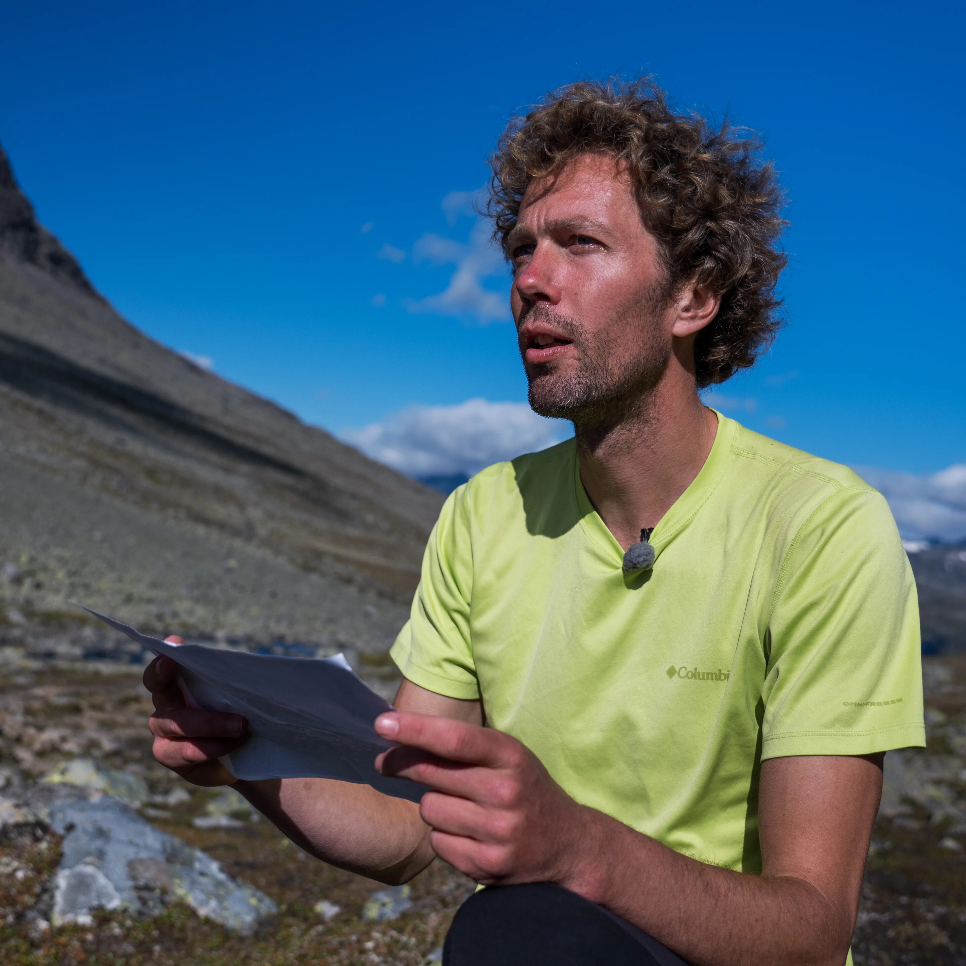 En mann ser på et ark og ut i fjellheimen