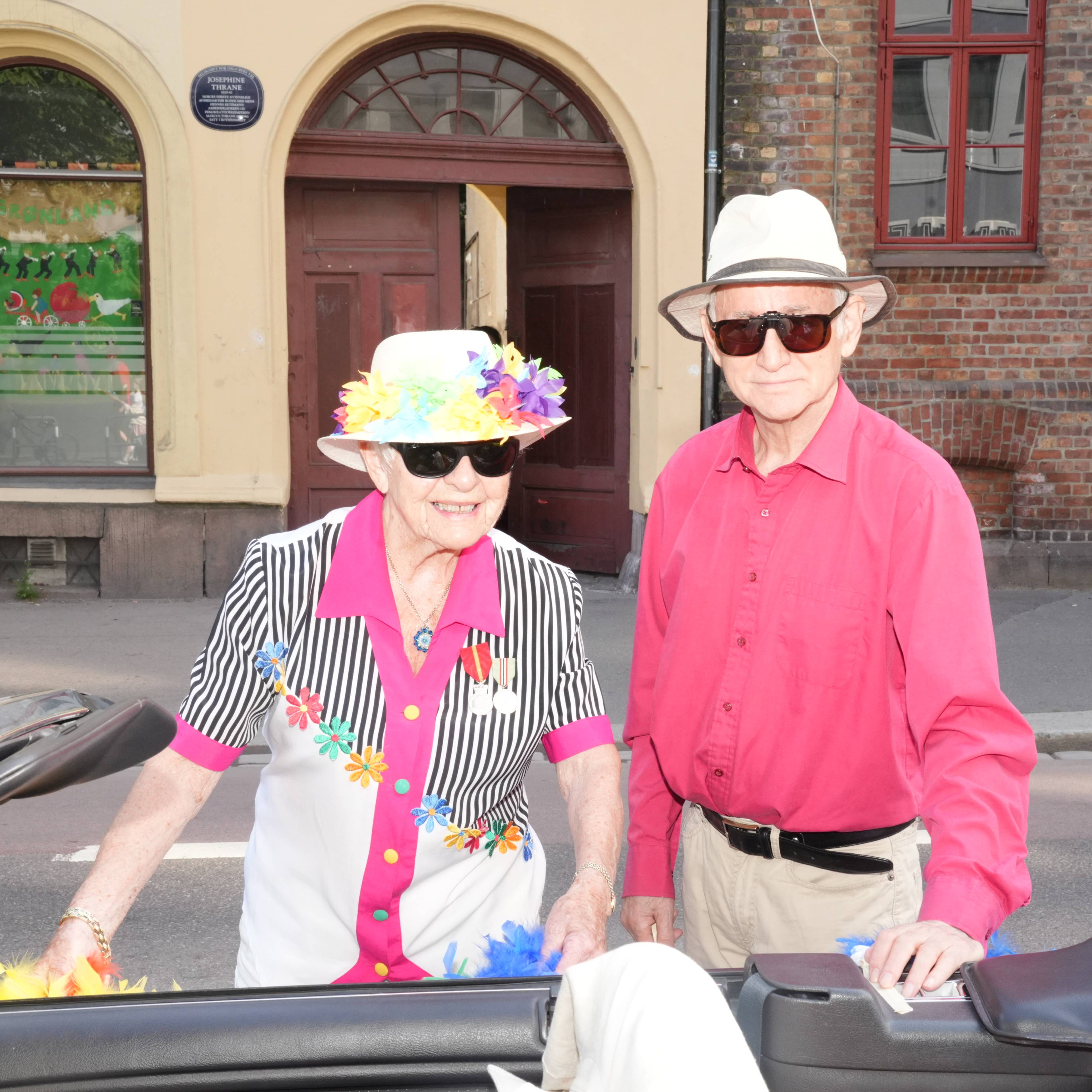 Bilde av to eldre personer med hatt som lener seg over en cabriolet.