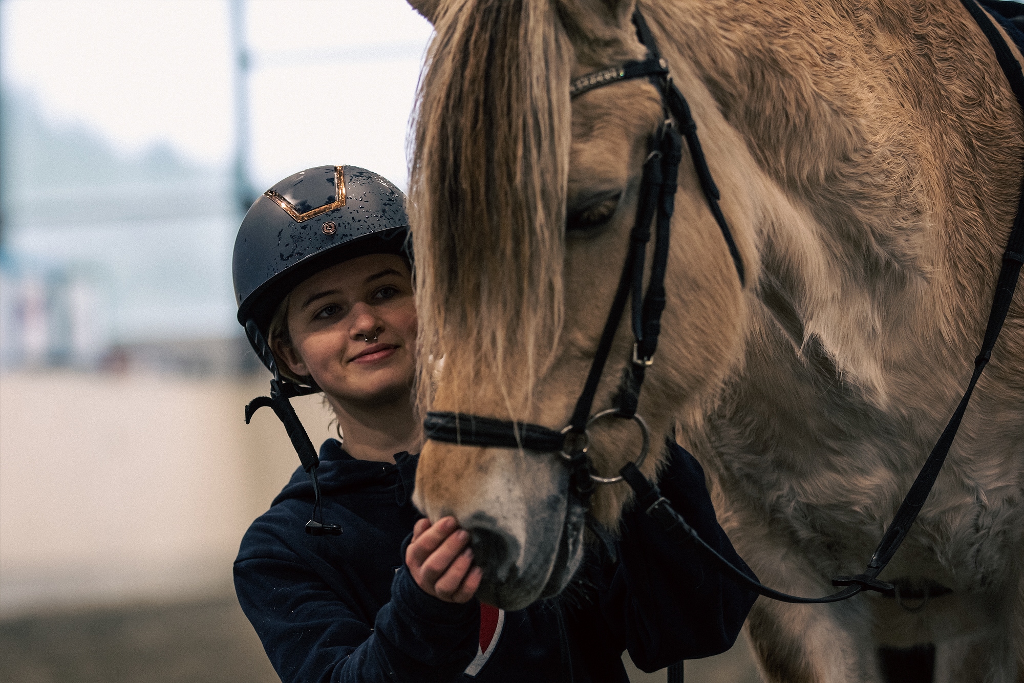 Bilde av Camilla sammen med hesten. Camilla smiler og har på seg en ridehjelm. 