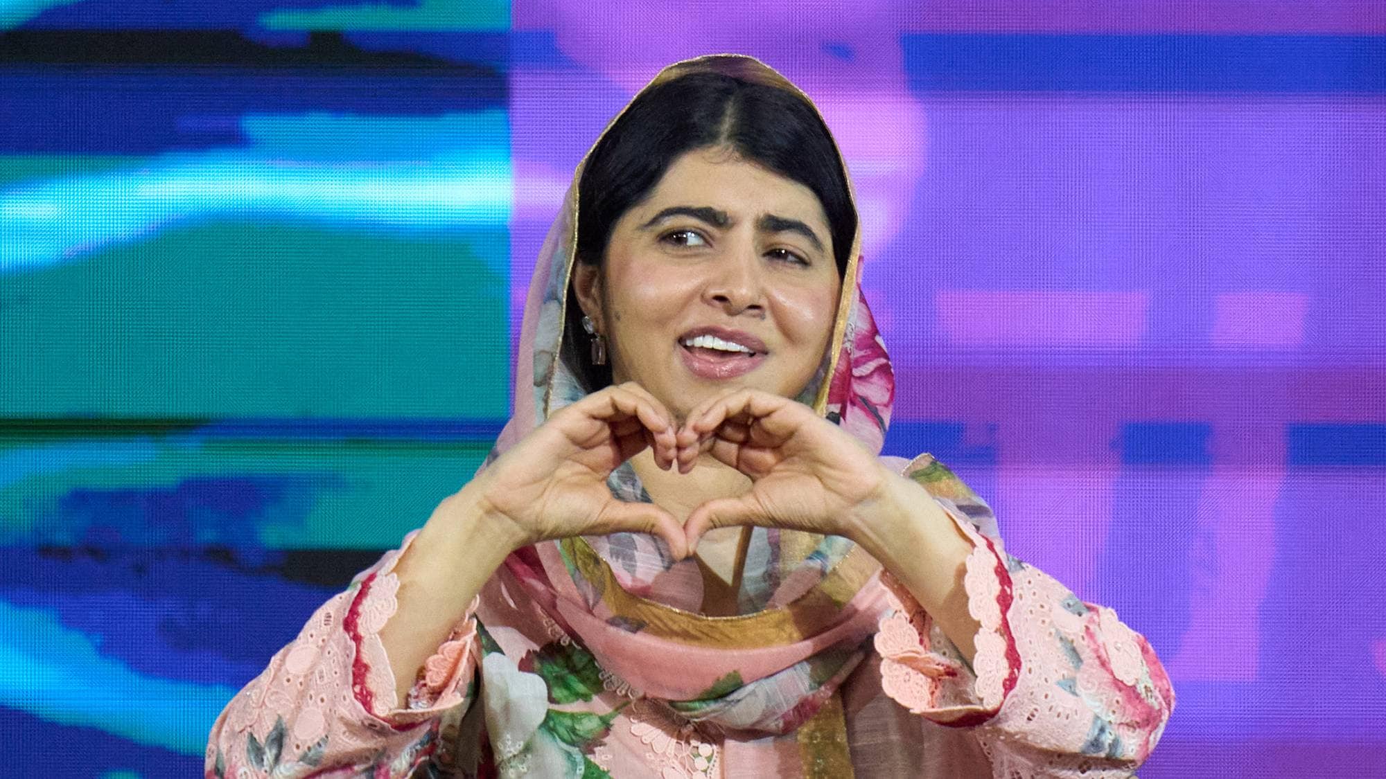 Malala Yousafzai sitter i en stol og danner et hjerte med hendene foran seg. (Bildebeskrivelsen er laget av en KI-tjeneste)