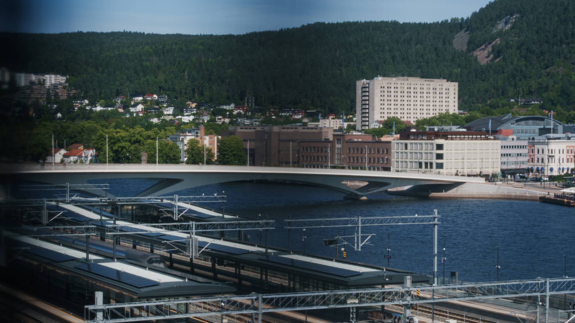 Bybro og togstasjon i Drammen med Drammenselva og bybebyggelse i bakgrunnen. (Bildebeskrivelsen er laget av en KI-tjeneste)