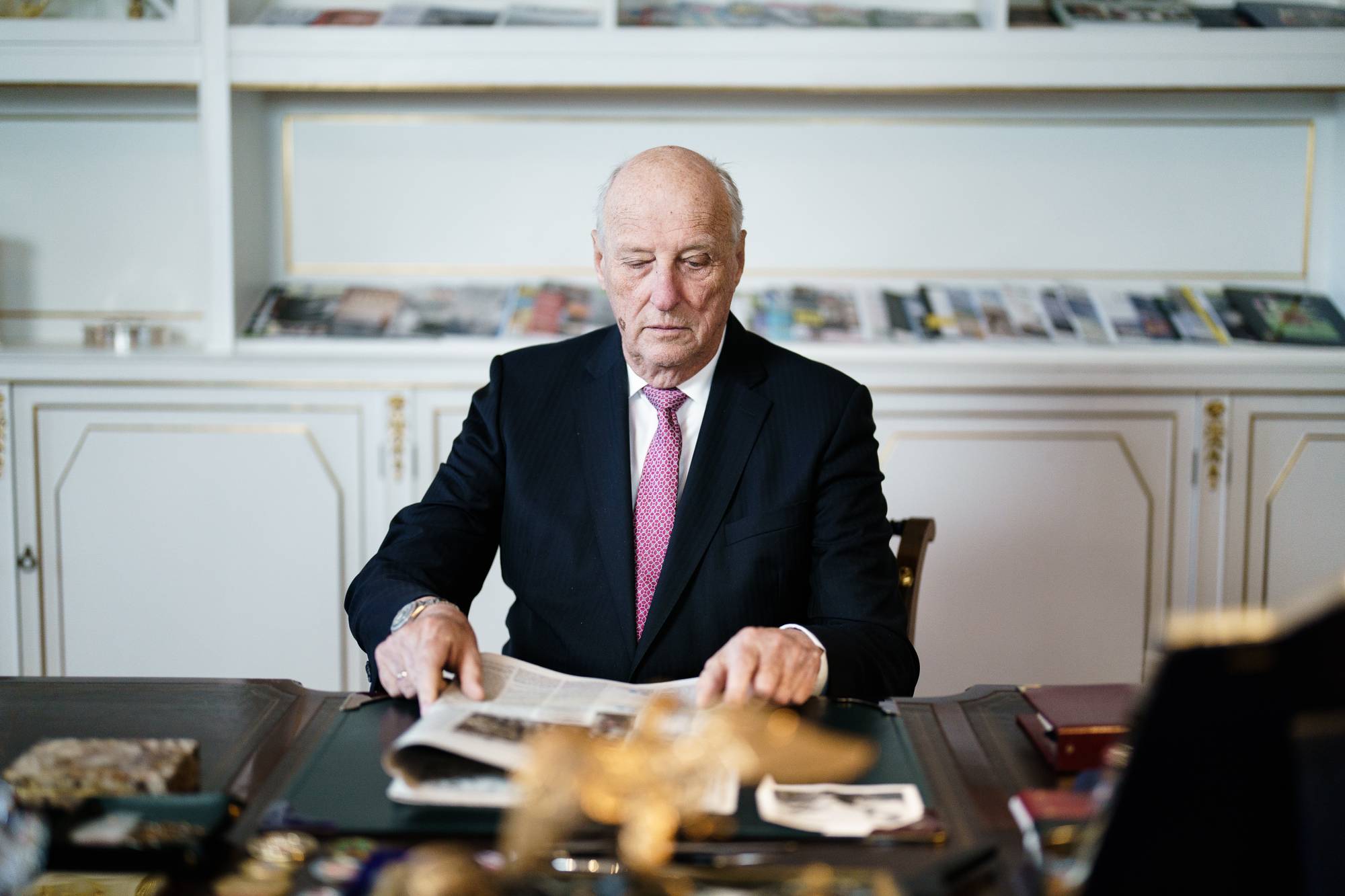 Kong Harald leser avisen ved skrivebordet på kontoret sitt på Slottet