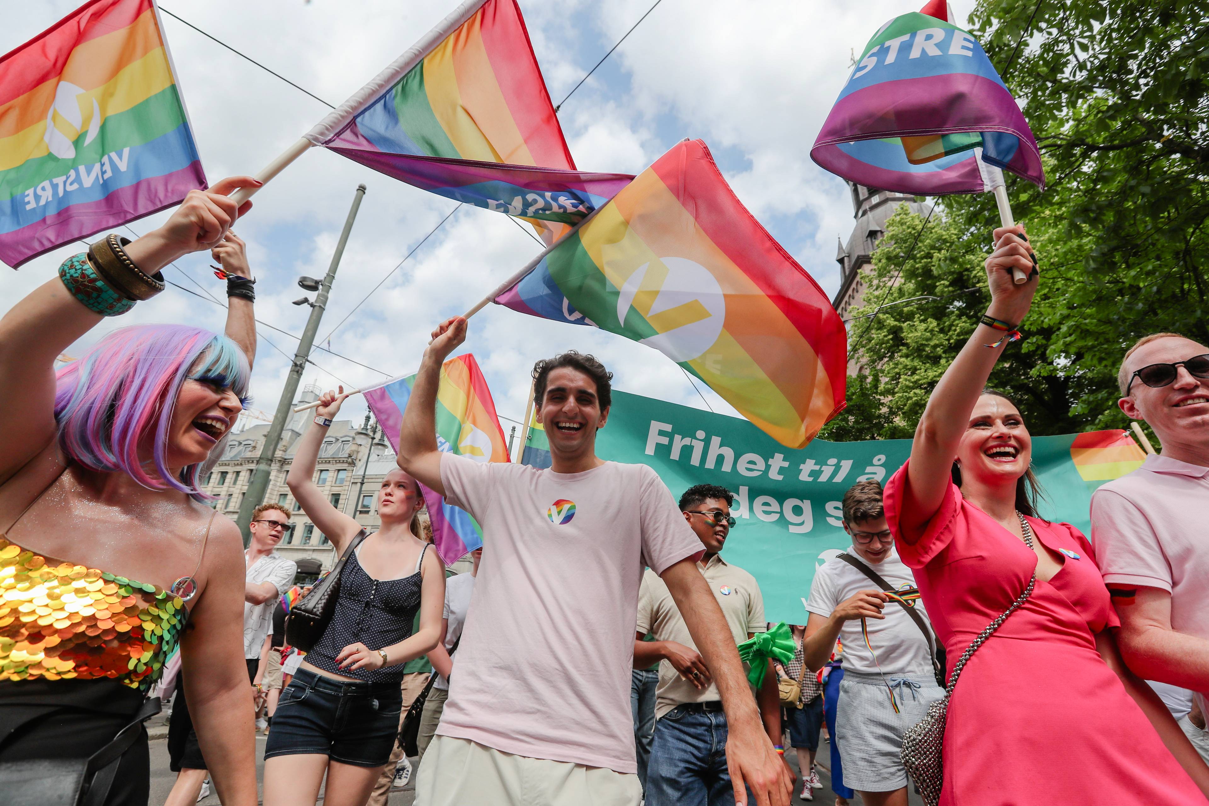 Folk går i pride-parade med regnbueflagg og en plakat med teksten Frihet til å være deg. (Bildebeskrivelsen er laget av en KI-tjeneste)