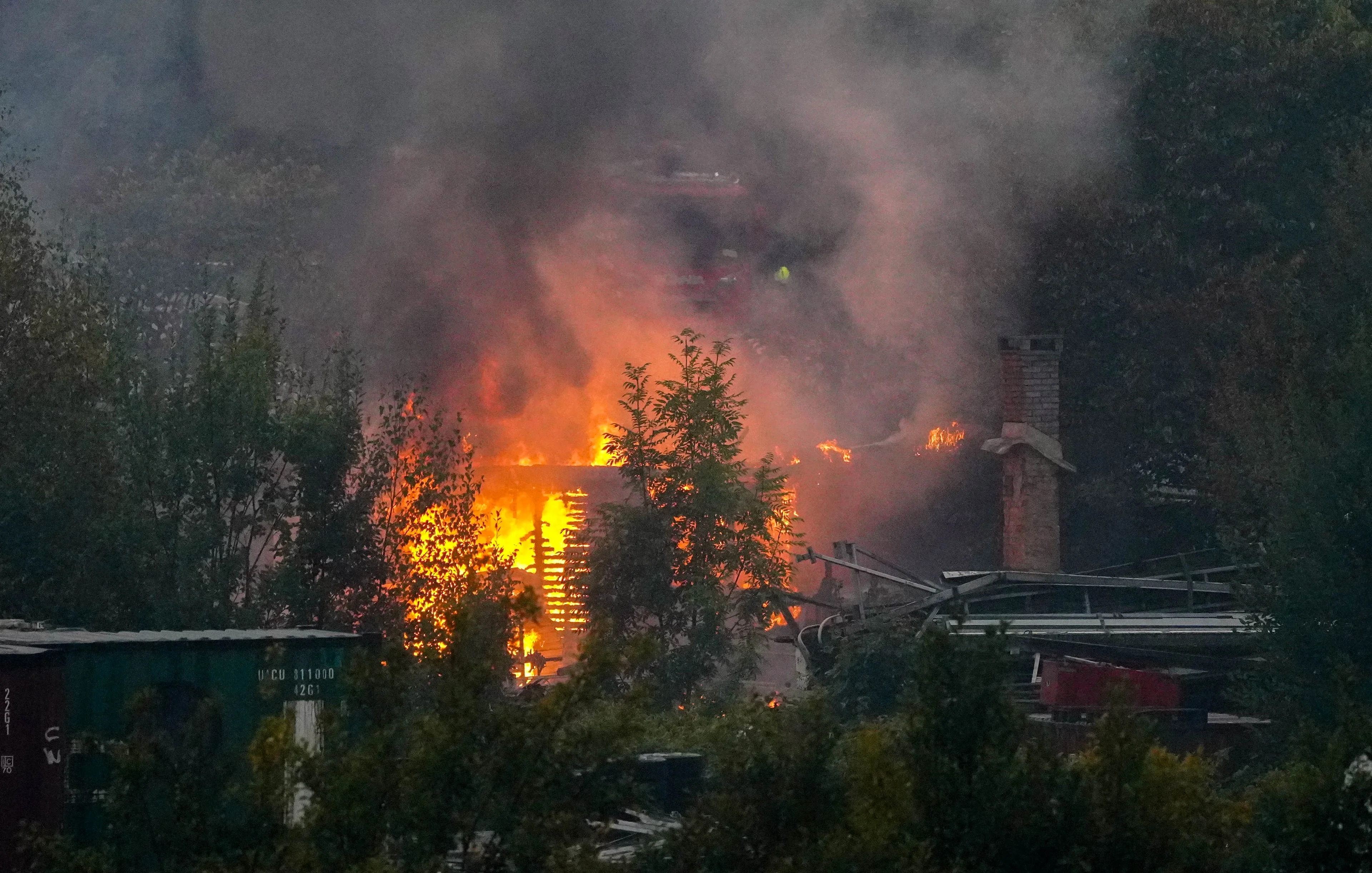 Kraftig brann i bygning omgitt av trær med synlig røyk og en brannbil i bakgrunnen. (Bildebeskrivelsen er laget av en KI-tjeneste)