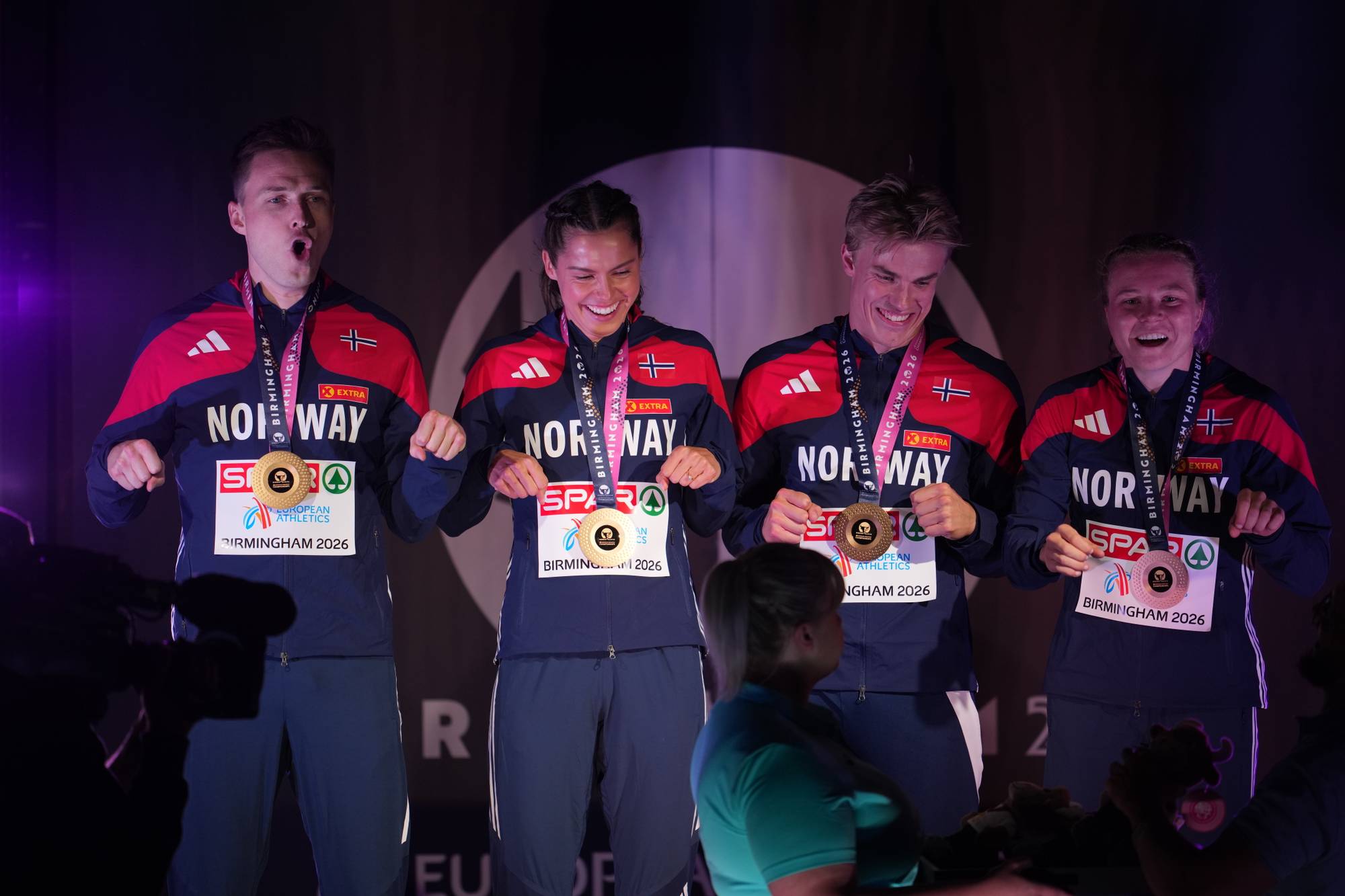 Fire norske utøvere i landslagsdrakter jubler med medaljer under premieutdeling i Birmingham. (Bildebeskrivelsen er laget av en KI-tjeneste)