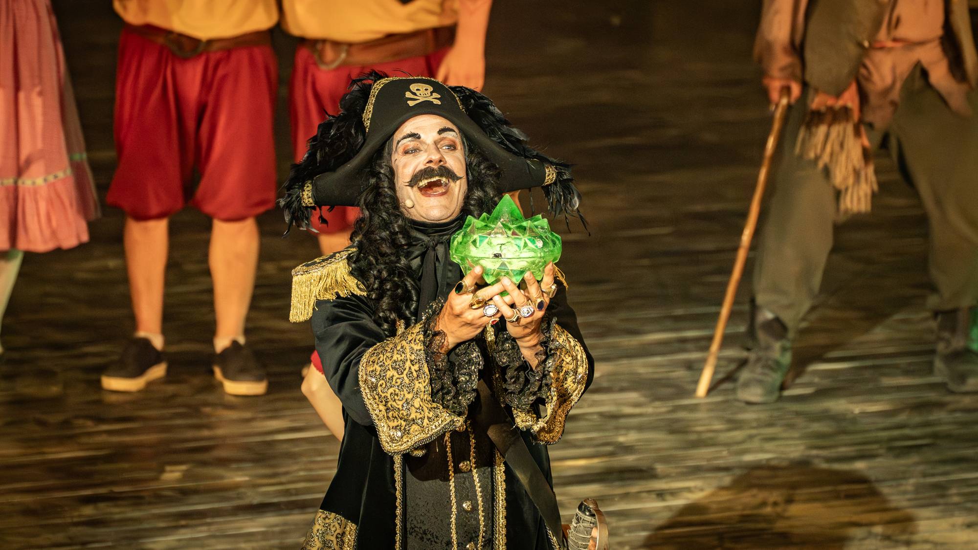 Skuespiller i piratkostyme holder en lysende grønn gjenstand på en scene. (Bildebeskrivelsen er laget av en KI-tjeneste)