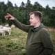 Benjamin Fredriksen / Benjamin Fredriksen / NRK En mann som peker oppover, i bakgrunnen er en saueflokk