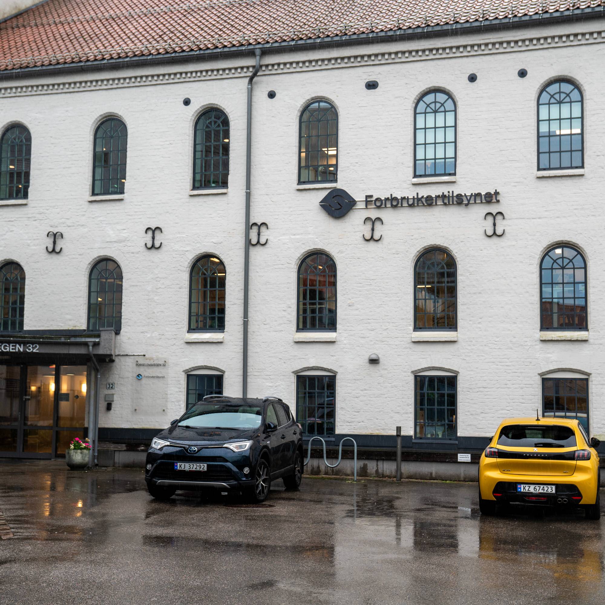 En bygning i mur der to biler står parkert foran.