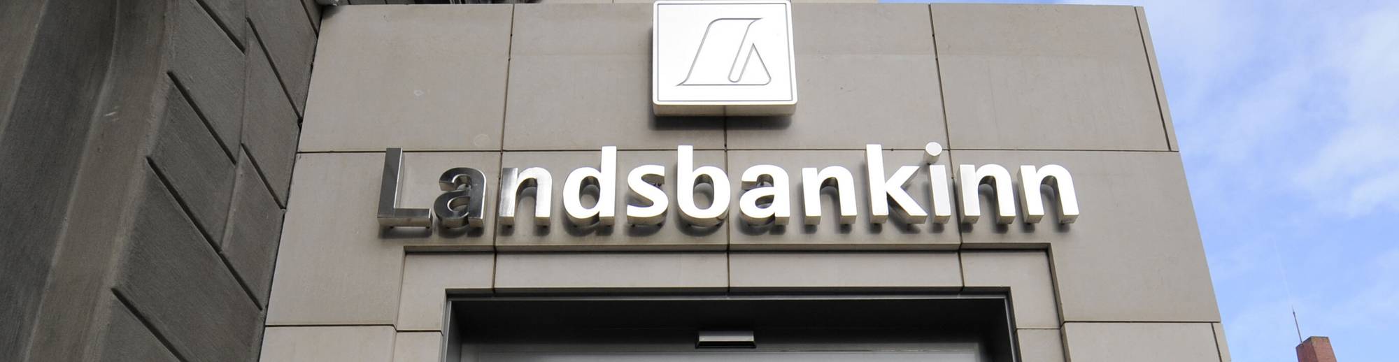 Person går inn inngangen til Landsbankinn i Reykjavik. Skilt med valutakurser står ved døren. (Bildebeskrivelsen er laget av en KI-tjeneste)