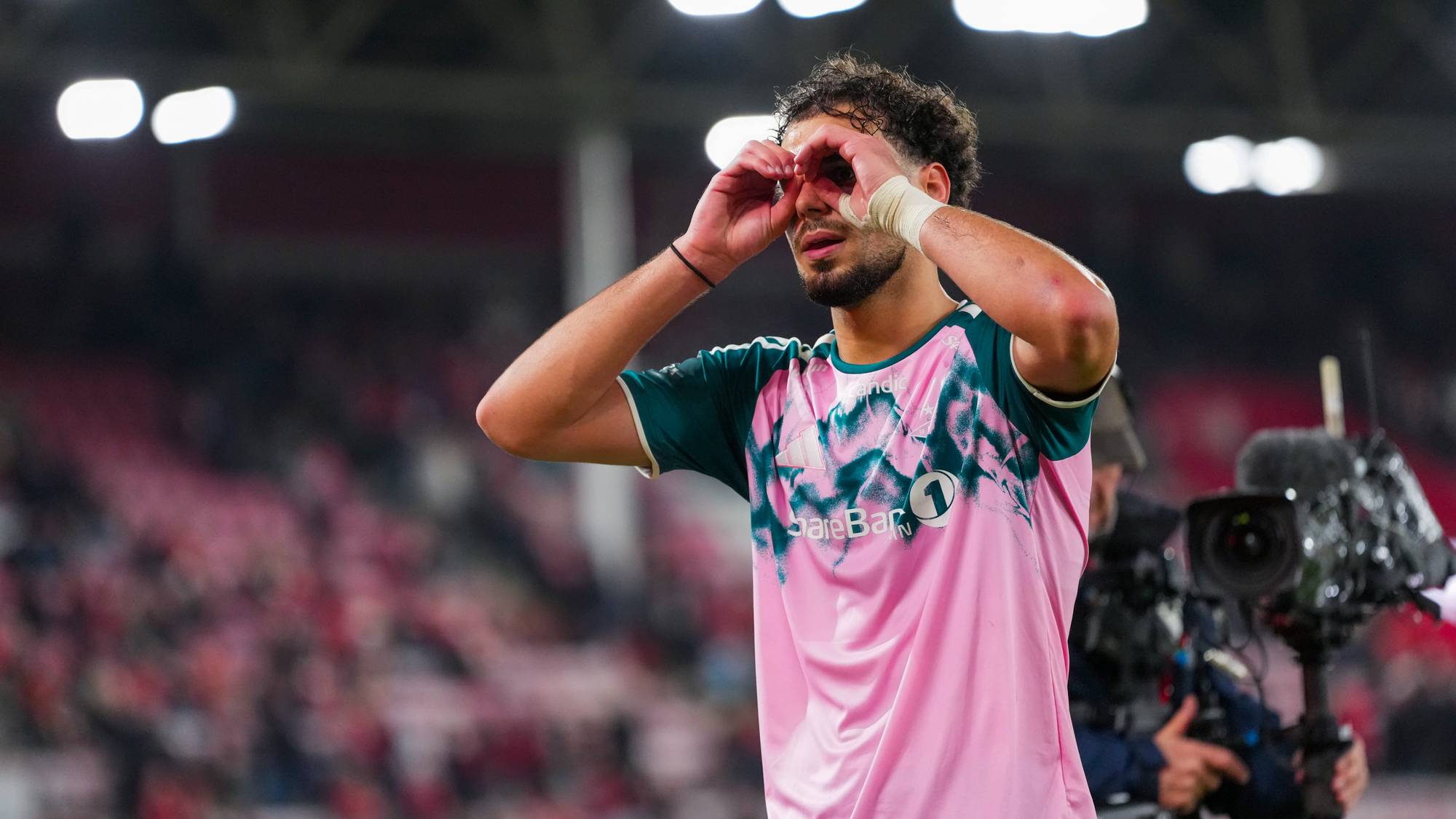 Fotballspiller i rosa drakt feirer med hendene som en kikkert foran øynene på en fotballstadion. (Bildebeskrivelsen er laget av en KI-tjeneste)