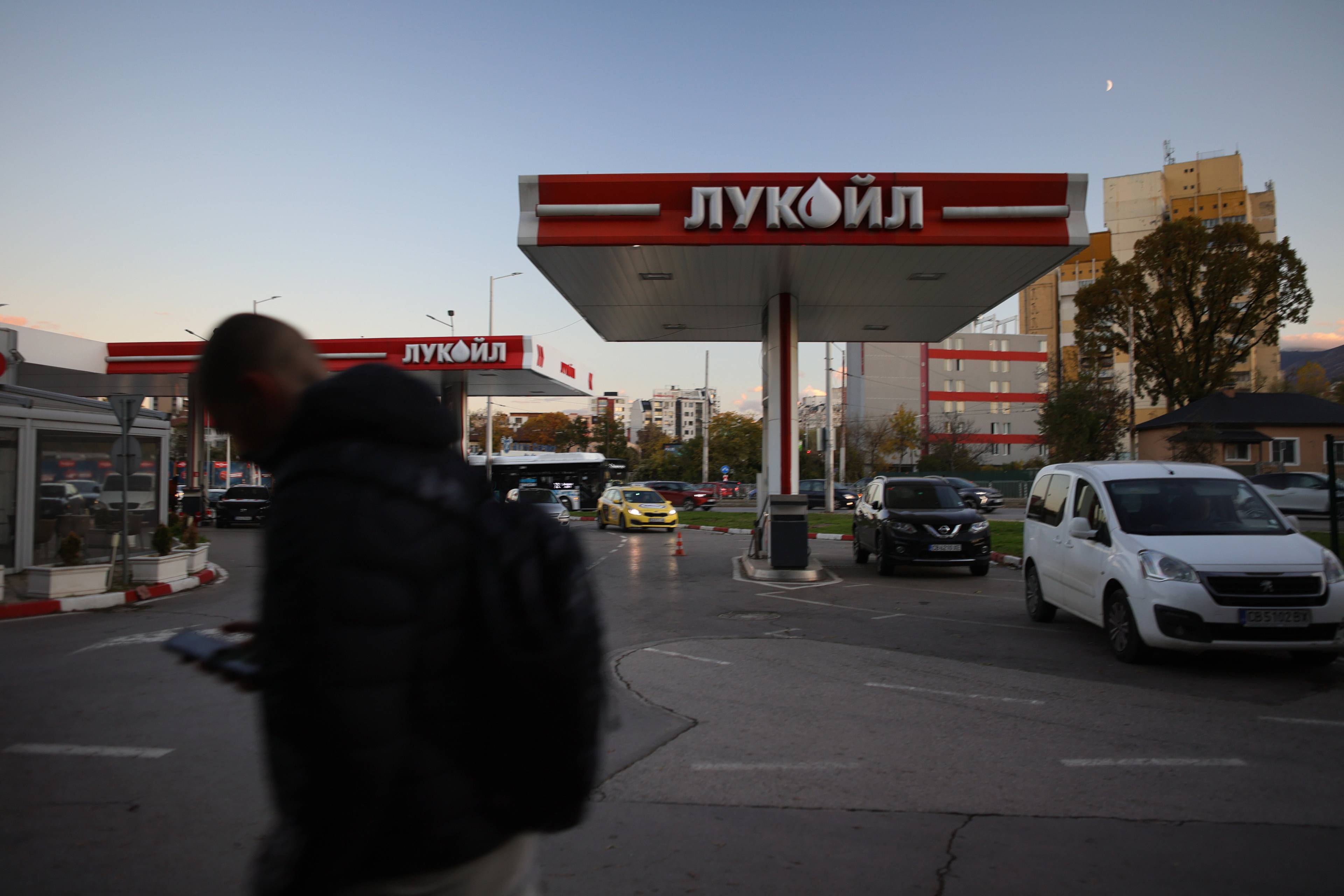 En bensinstasjon med Lukoil-logo. Person i forgrunnen og biler ved pumpene i bymiljø. (Bildebeskrivelsen er laget av en KI-tjeneste)