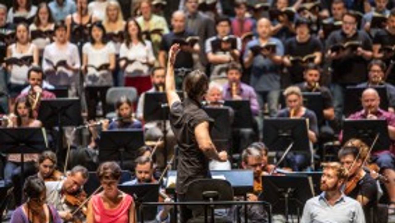 Teodor Currentzis med ryggen til, musikere i fargerike klær i bakgrunnen