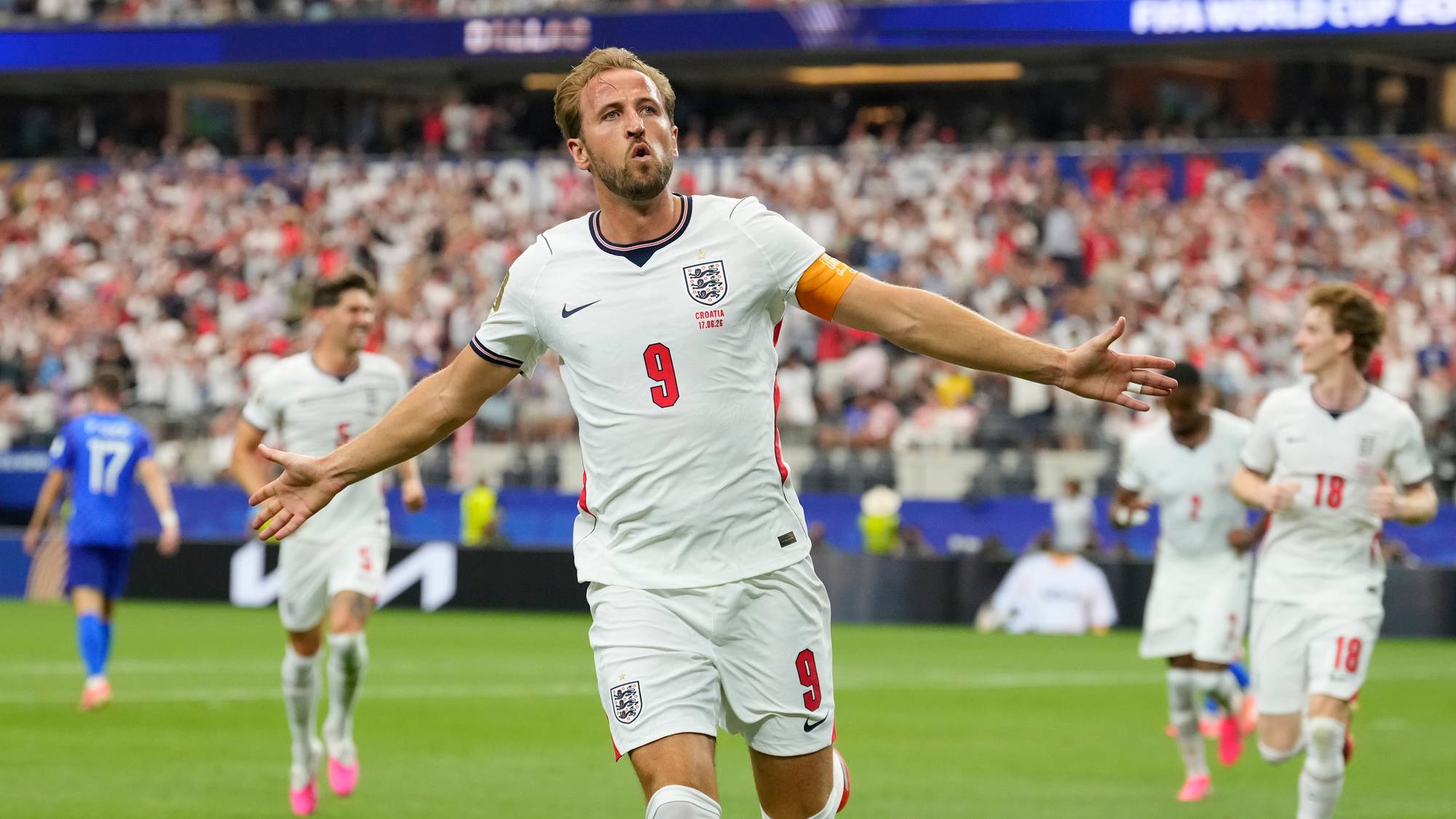 Harry Kane jubler for England på en fotballbane med lagkamerater i bakgrunnen. (Bildebeskrivelsen er laget av en KI-tjeneste)