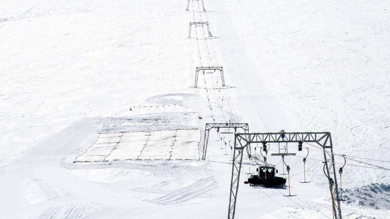 Bildet viser hele skisenteret til Per Arne Vole på Vesl-Juvbrean i Lom. Sola skinner. Man ser mastene som skiheisen går oppover gjennom til høyre i bildet. Under ene masten kan man se tråkkemaskinen. Midt i bildet ligger det fire hvite duker som er lagt over breen for å bevare snøen gjennom sommeren. 