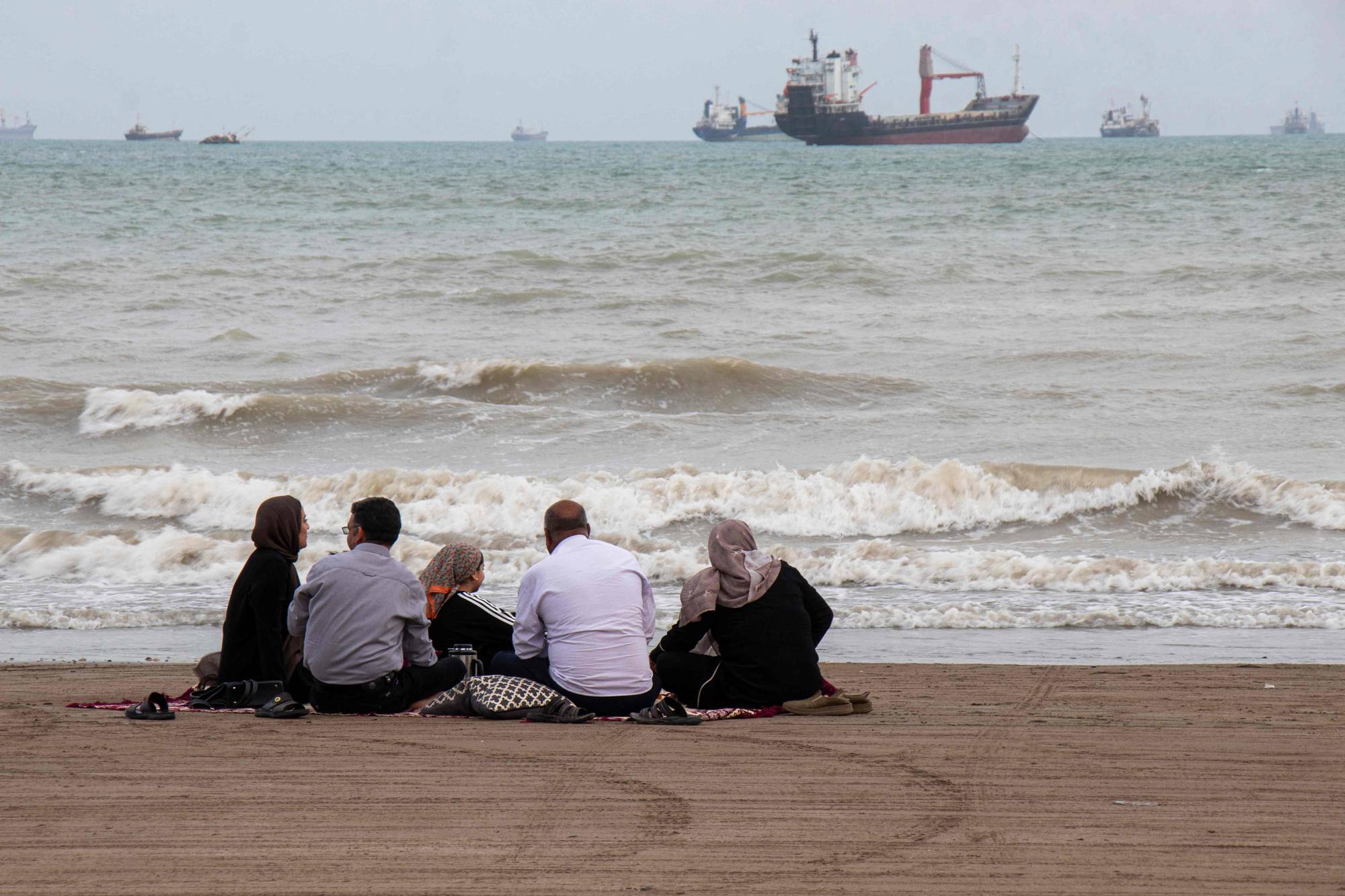 En iransk familie sitter på stranden ved Hormuzstredet 
