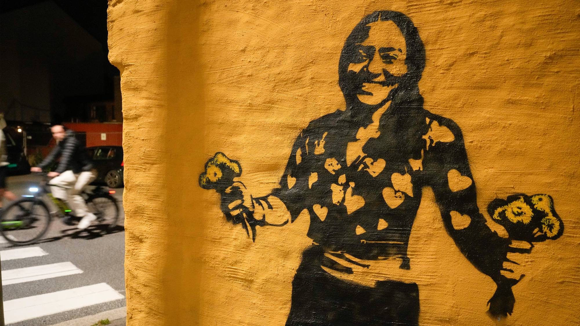 Grafitti av en smilende person med blomster malt på en gul vegg i et bymiljø. 