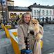 Kristoffer Edvardsen / NRK En person i beige frakk står på en fortau med en pomeranianhund i armene. Bakgrunnen viser bygninger med varierende arkitektur og en rekke uteplasser. Det er en klar dag med sollys, og noen sykler står parkert i nærheten. Området ser ut til å være et offentlig sted med sitteplasser og grøntarealer.