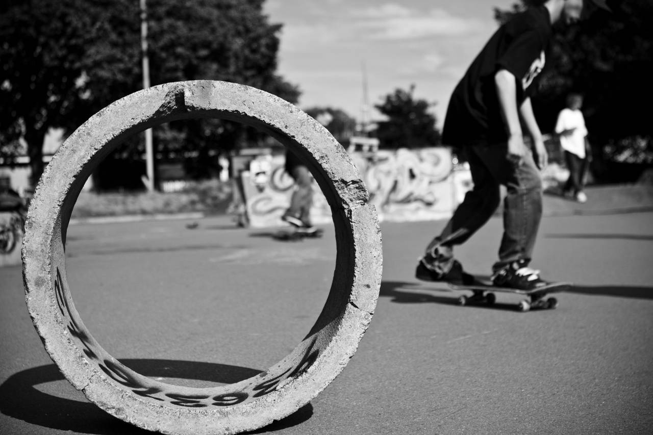 En betongring ligger på siden, så vi kan se gjennom den. I bakgrunnen skater Einar Andrésen og flere andre.