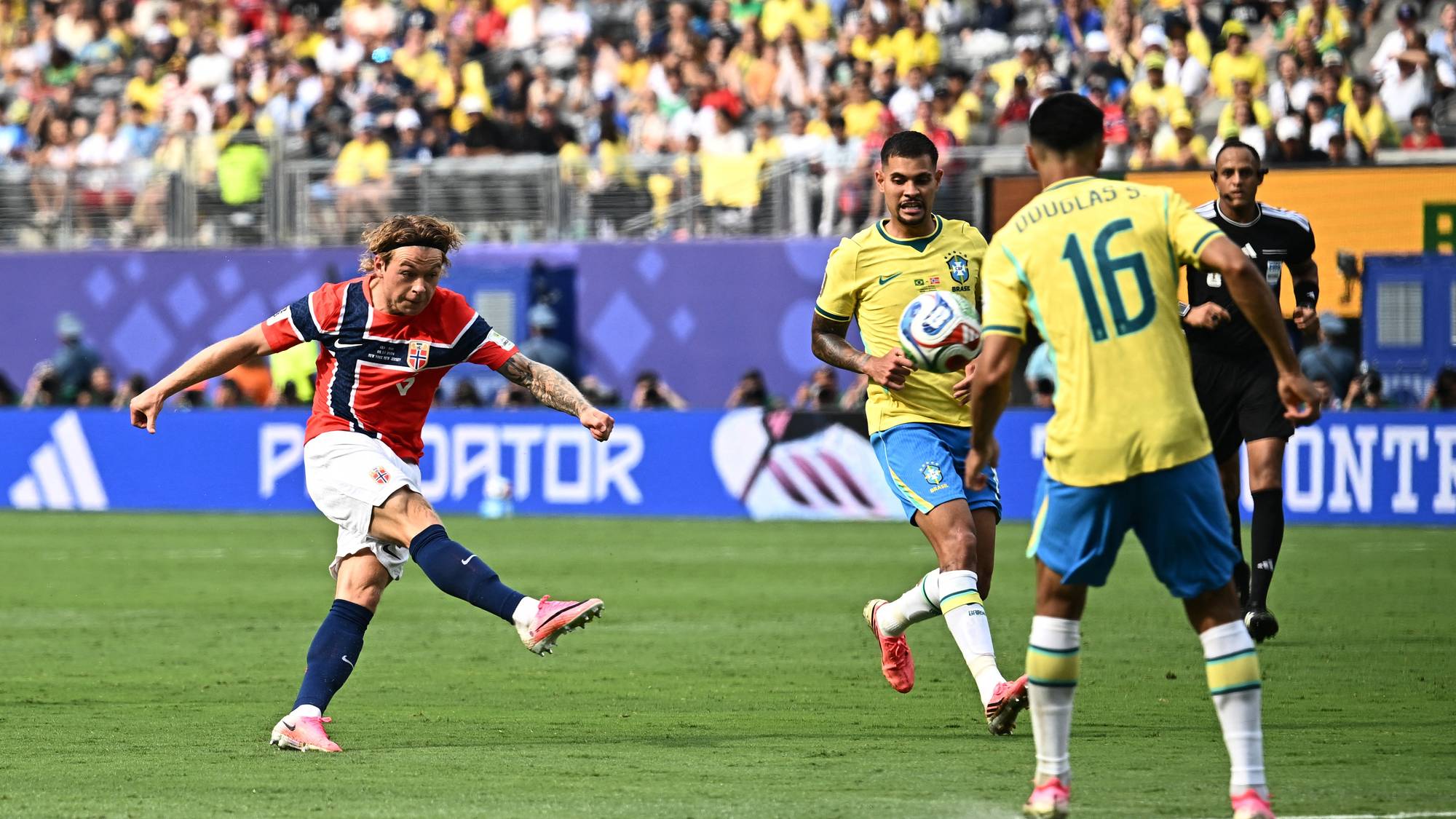 Norsk spiller i rød drakt skyter ballen foran brasilianske spillere på gressbane. (Bildebeskrivelsen er laget av en KI-tjeneste)