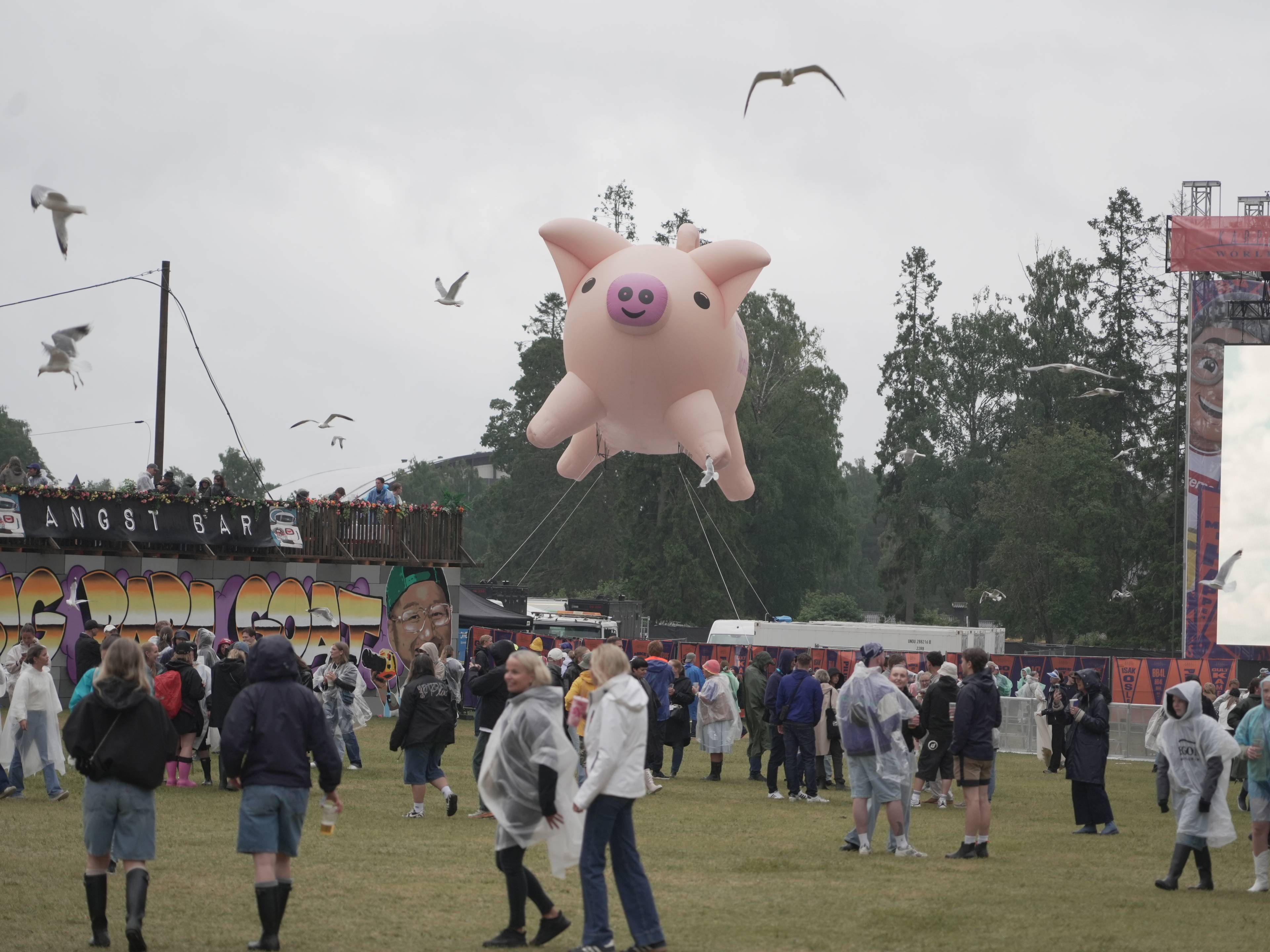 Stor oppblåsbar rosa gris svever over festivalområde med publikum, måker og en scene i bakgrunnen. (Bildebeskrivelsen er laget av en KI-tjeneste)