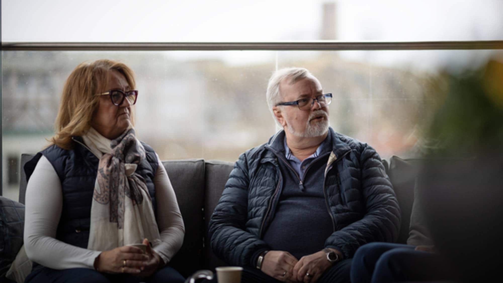 Erik Furevik og Berit Sæther Carlberg ser vekk fra kamera til høyre. De sitter på en balkong. Bakgrunnen bak dem er dus. 
