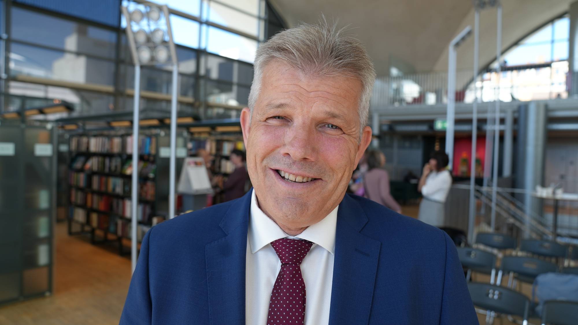 En mann i blå dress i halvnært portrett på et bibliotek
