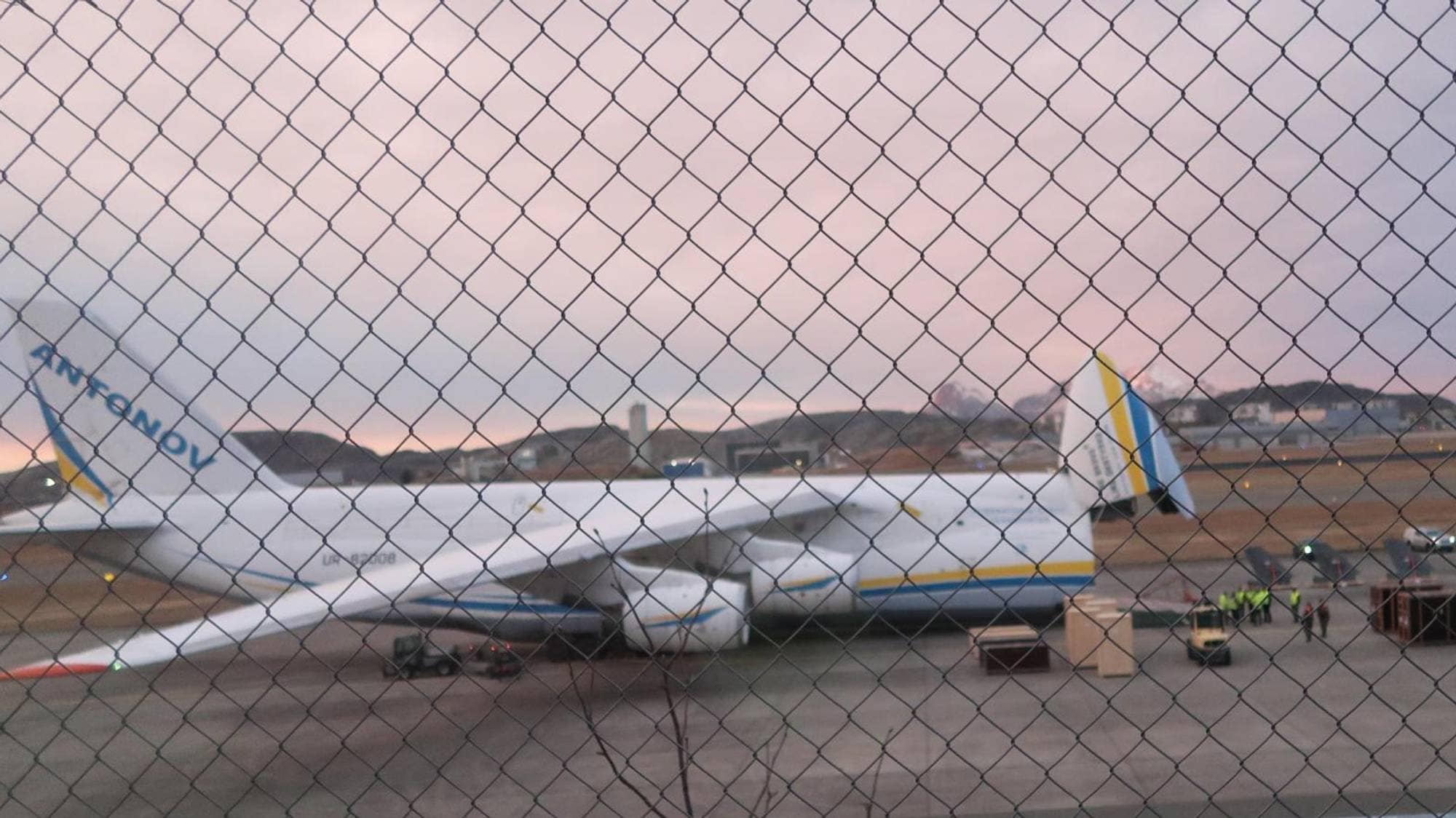Et veldig stort hvitt transportfly med påskriften ANTONOV sees med nesen av flyet vippet opp. Foran flyet står flere halefinner fra jagerfly klare for å lastes inn i hullet der nesen er vippet opp.