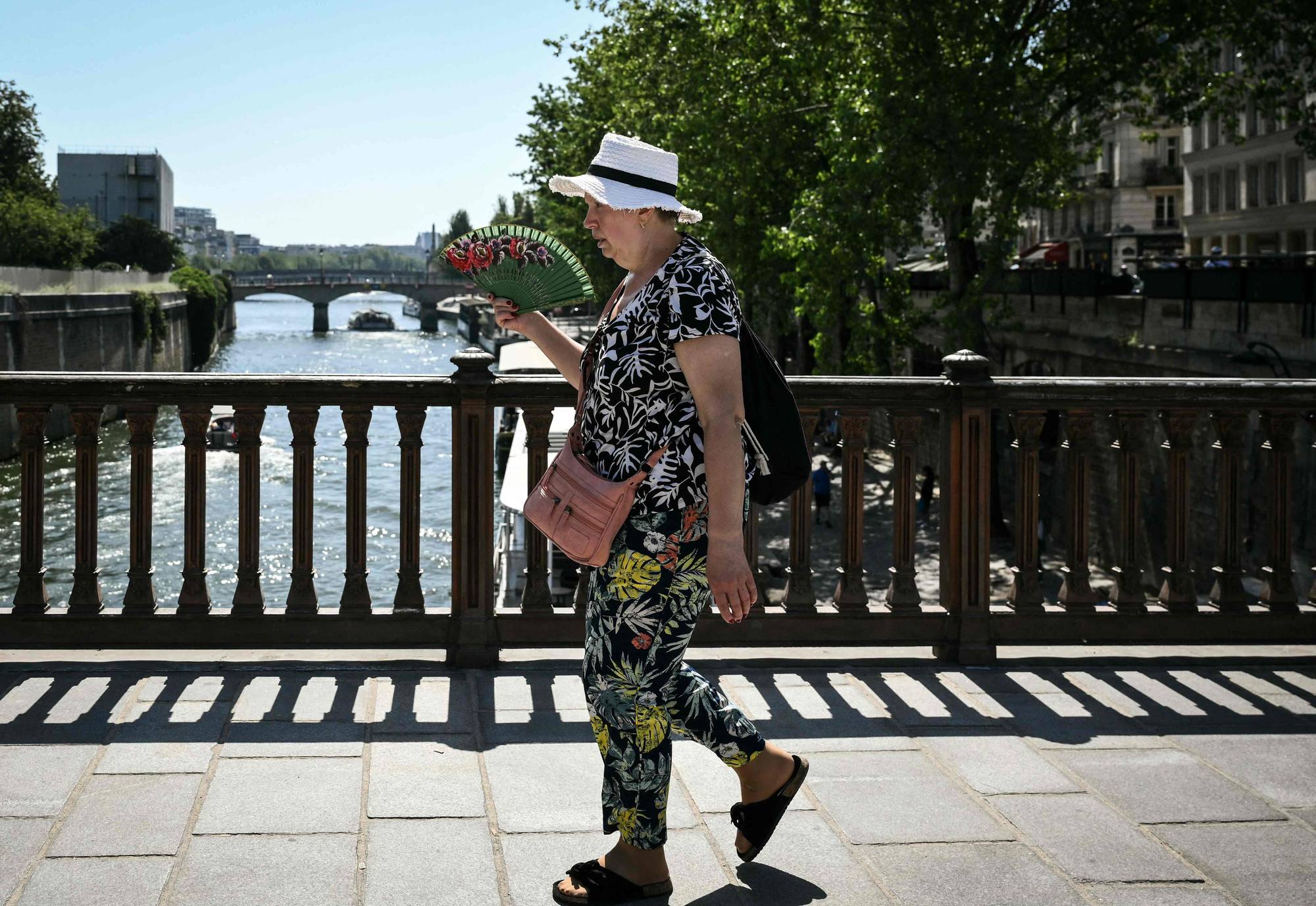 En kvinne kjøler seg ned med håndholdt vifte på en bro i Paris.