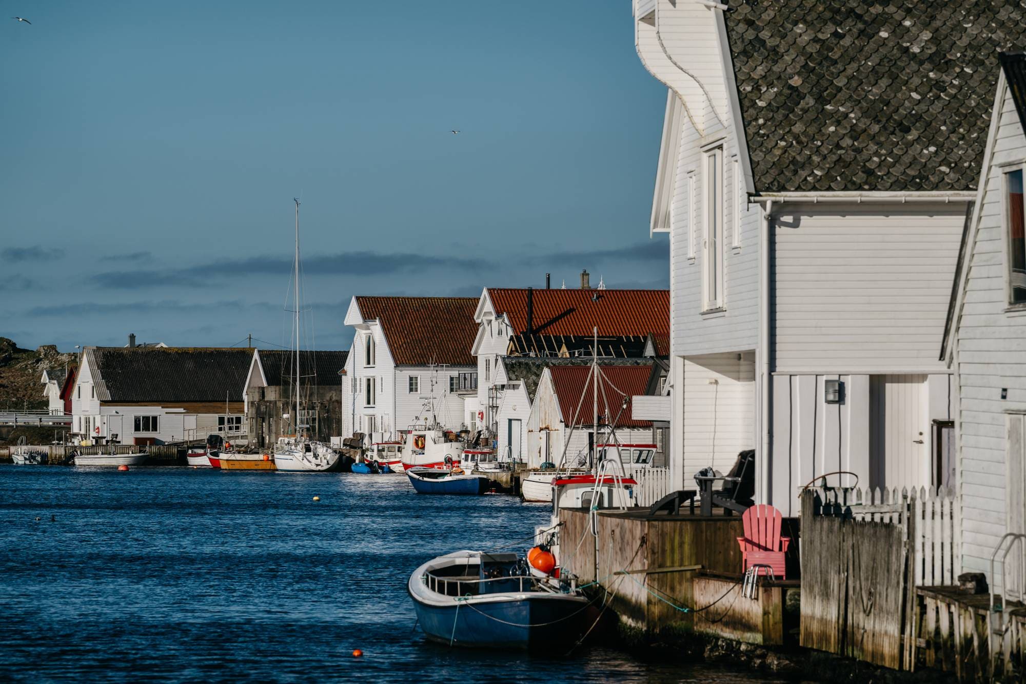 Hvite hus og sjøhus lags en brygge der det ligger fiskebåter.