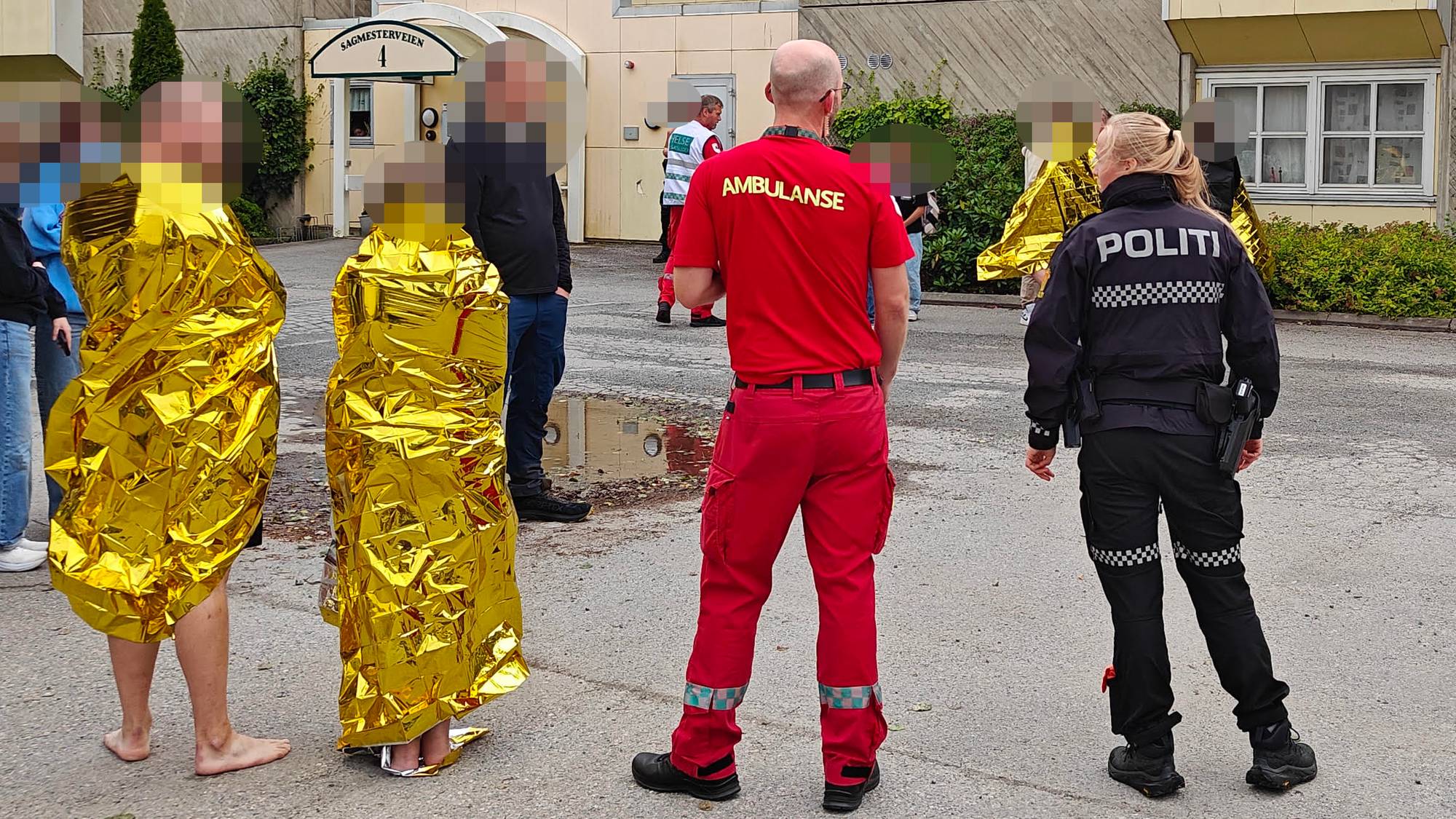 Flere badegjester iført folie etter evakuering fra badeland. Ambulansepersonell og politi står ved siden av dem