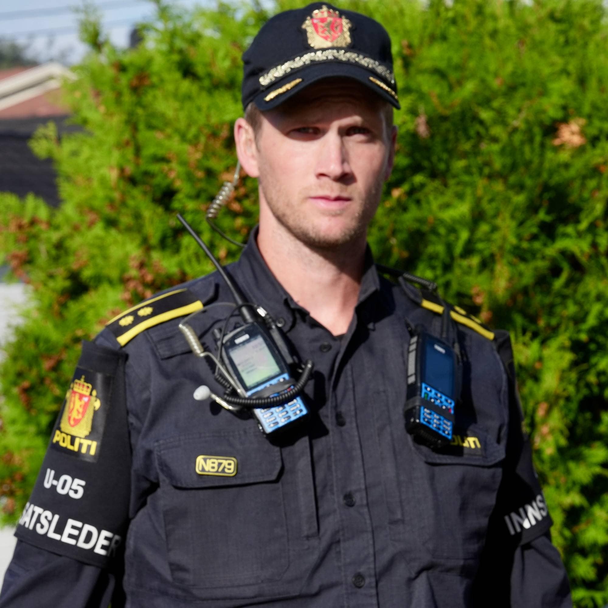 En politiinnsatsleder i uniform står utendørs foran en hekk. (Bildebeskrivelsen er laget av en KI-tjeneste)